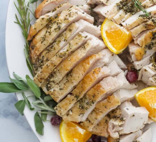 roasted turkey breast that's been sliced on a plate with herbs and orange wedges