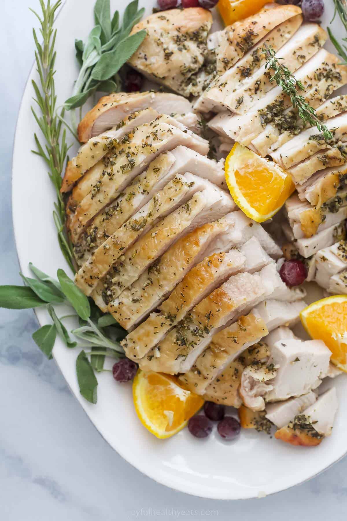 roasted turkey breast that's been sliced on a plate with herbs and orange wedges