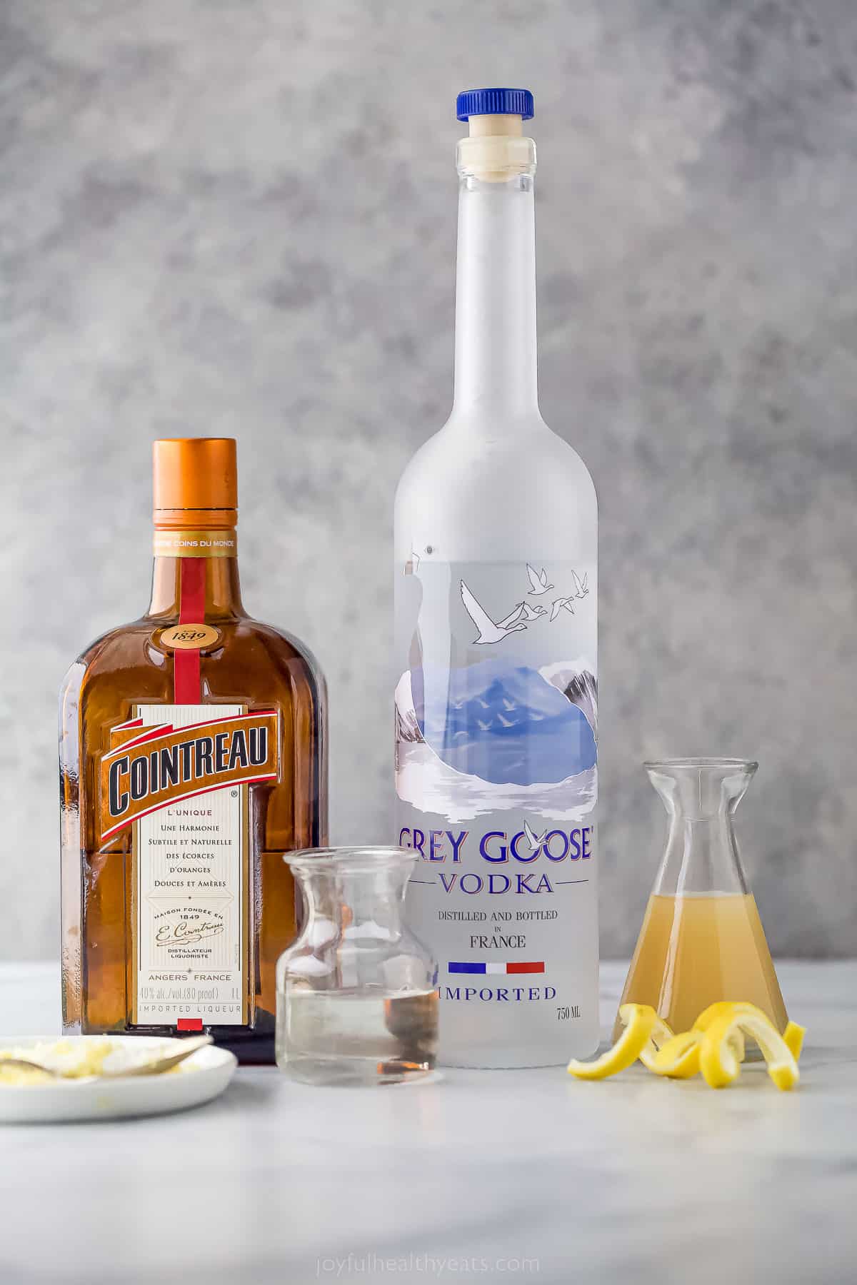 Bar ingredients to make a lemon drop martini including vodka, lemon juice, lemon peels, and Cointreau