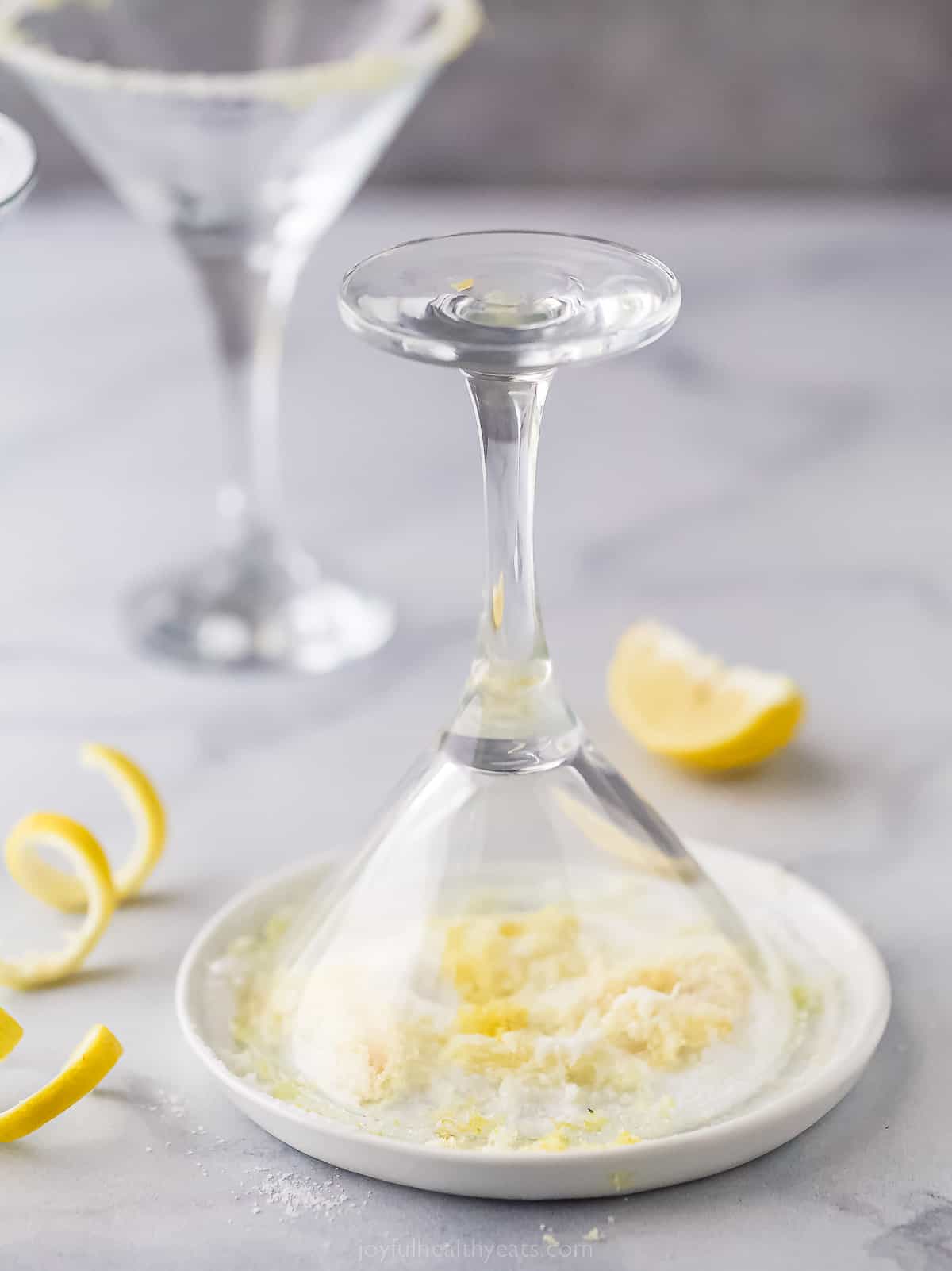 dipping a martini glass upside down into a plate with sugar to make a sugared rim