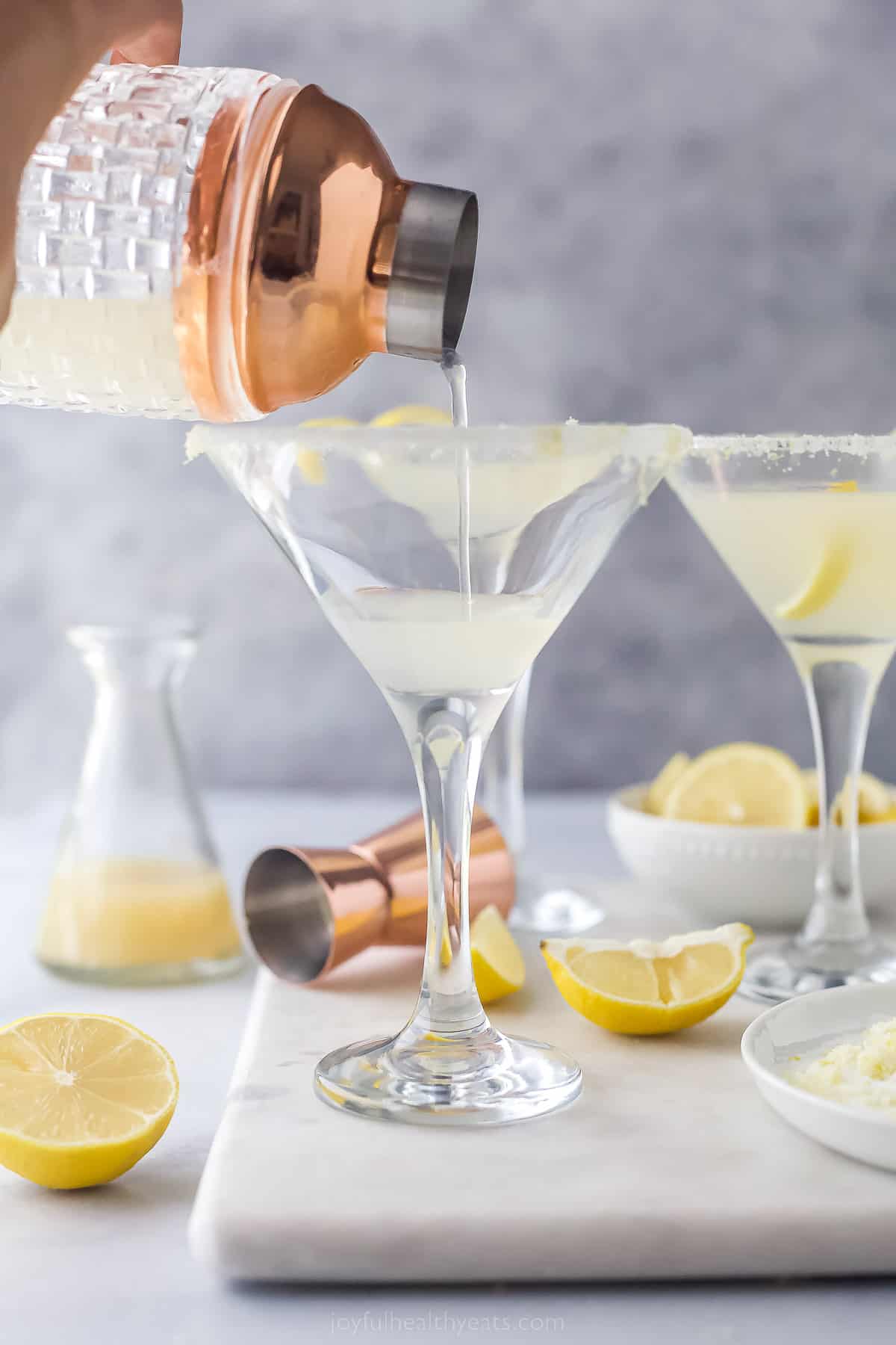 a cocktail shaker pouring a drink into a martini glass with sugared rim