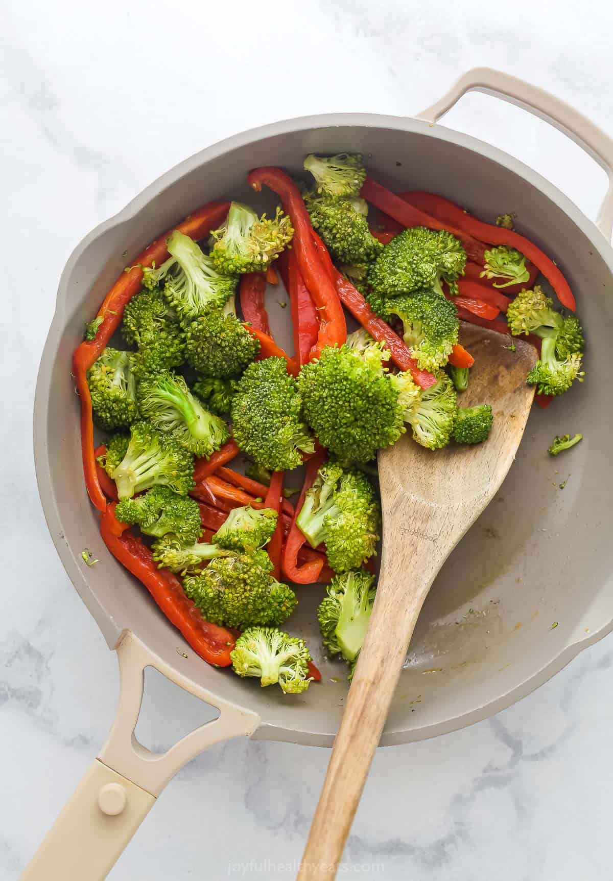 a saute pan with sliced red peppers and broccoil