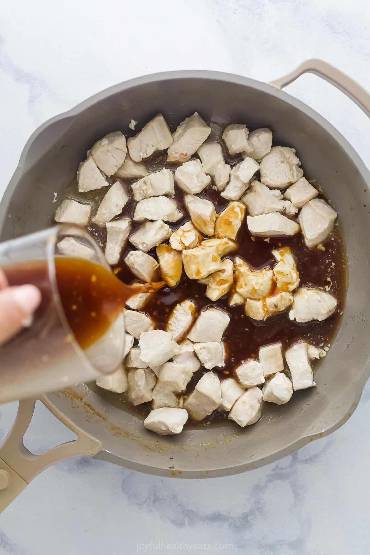 pouring a brown stir fry sauce into a saute pan with chicken pieces