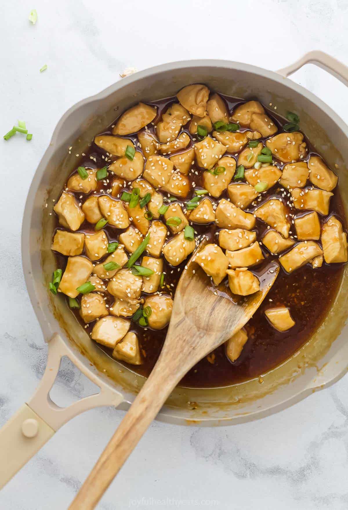 chicken pieces being mixed with teriyaki sauce in a saute pan