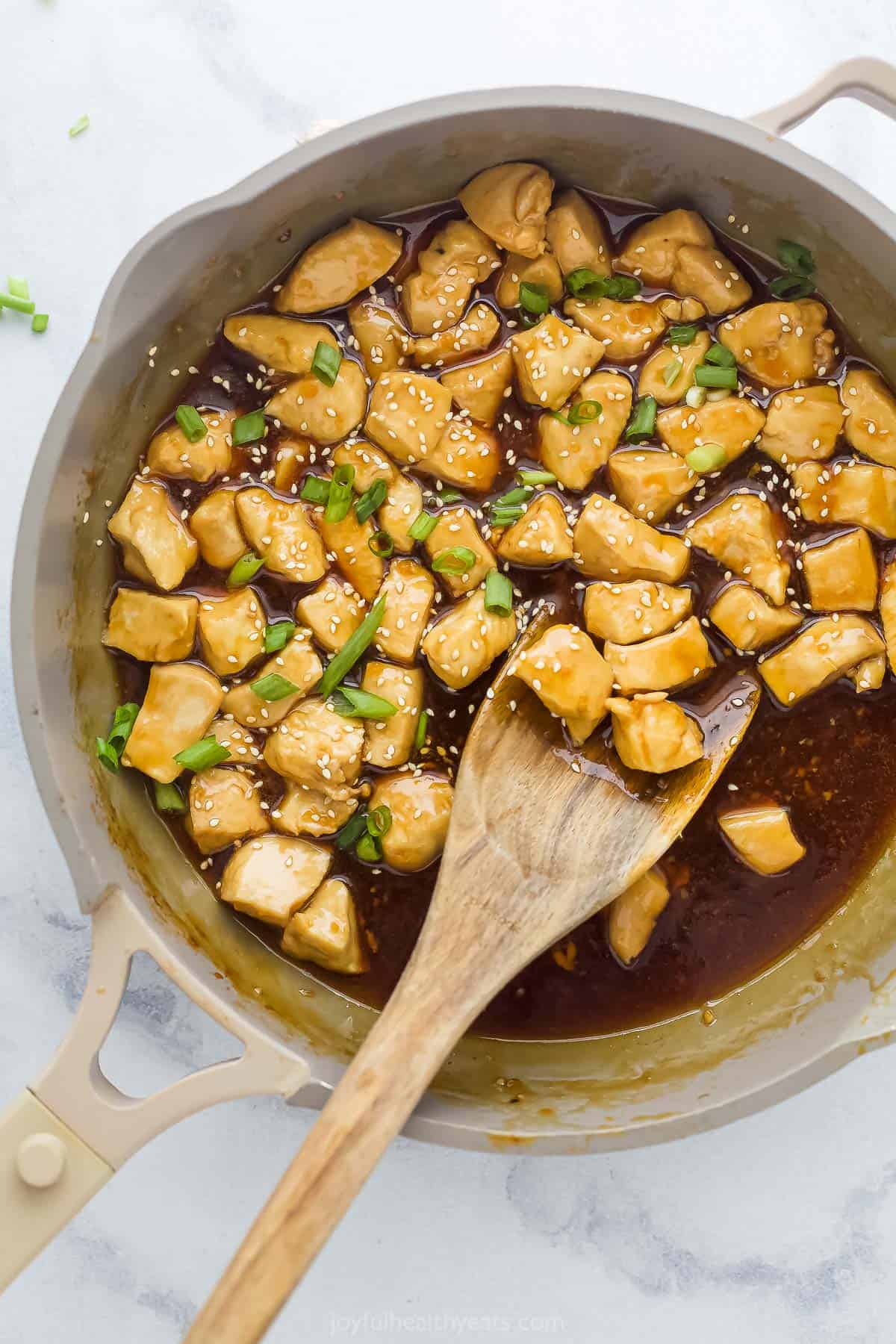 chicken pieces being mixed with teriyaki sauce in a saute pan