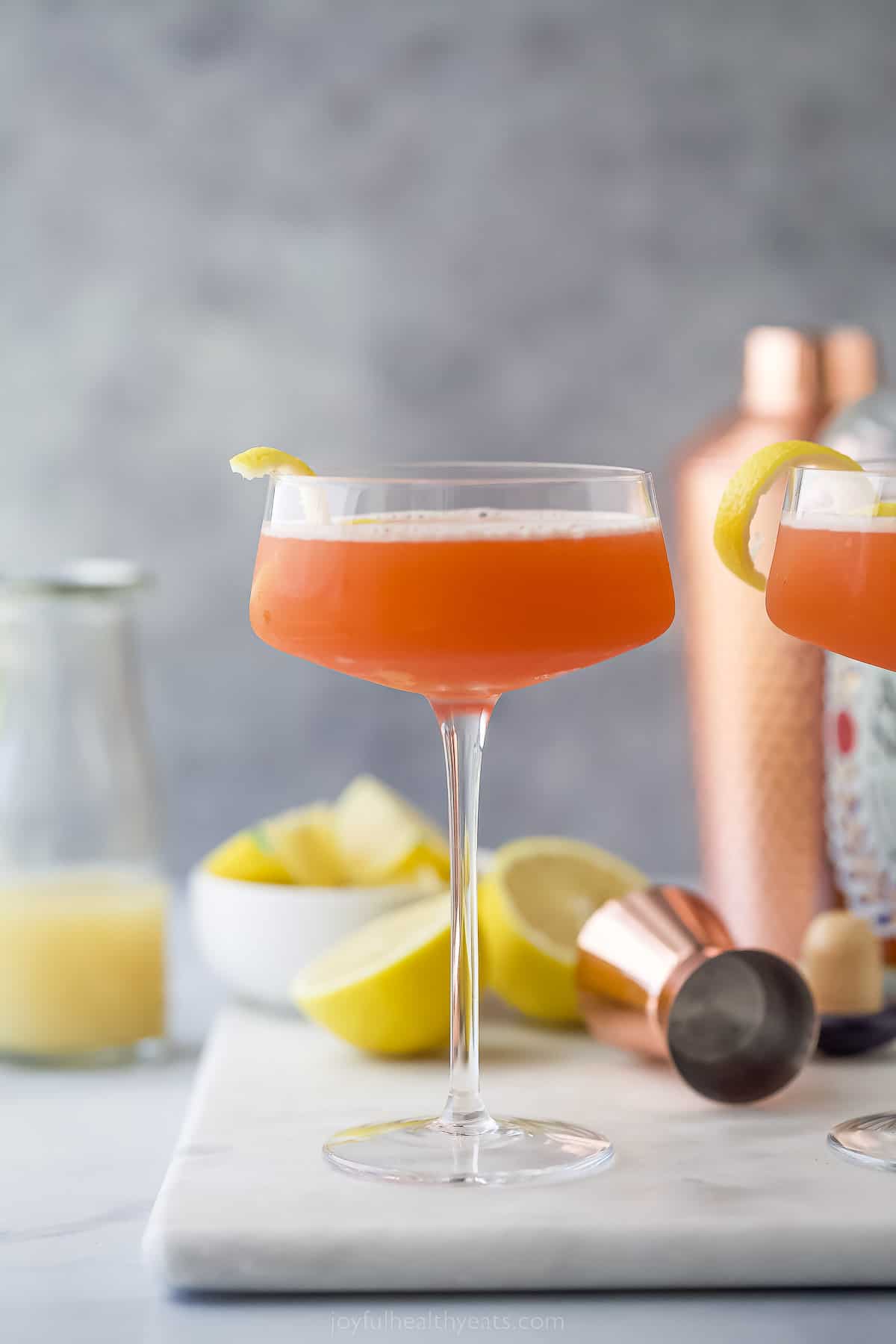 A pale orange paper plane drink with lemon garnish