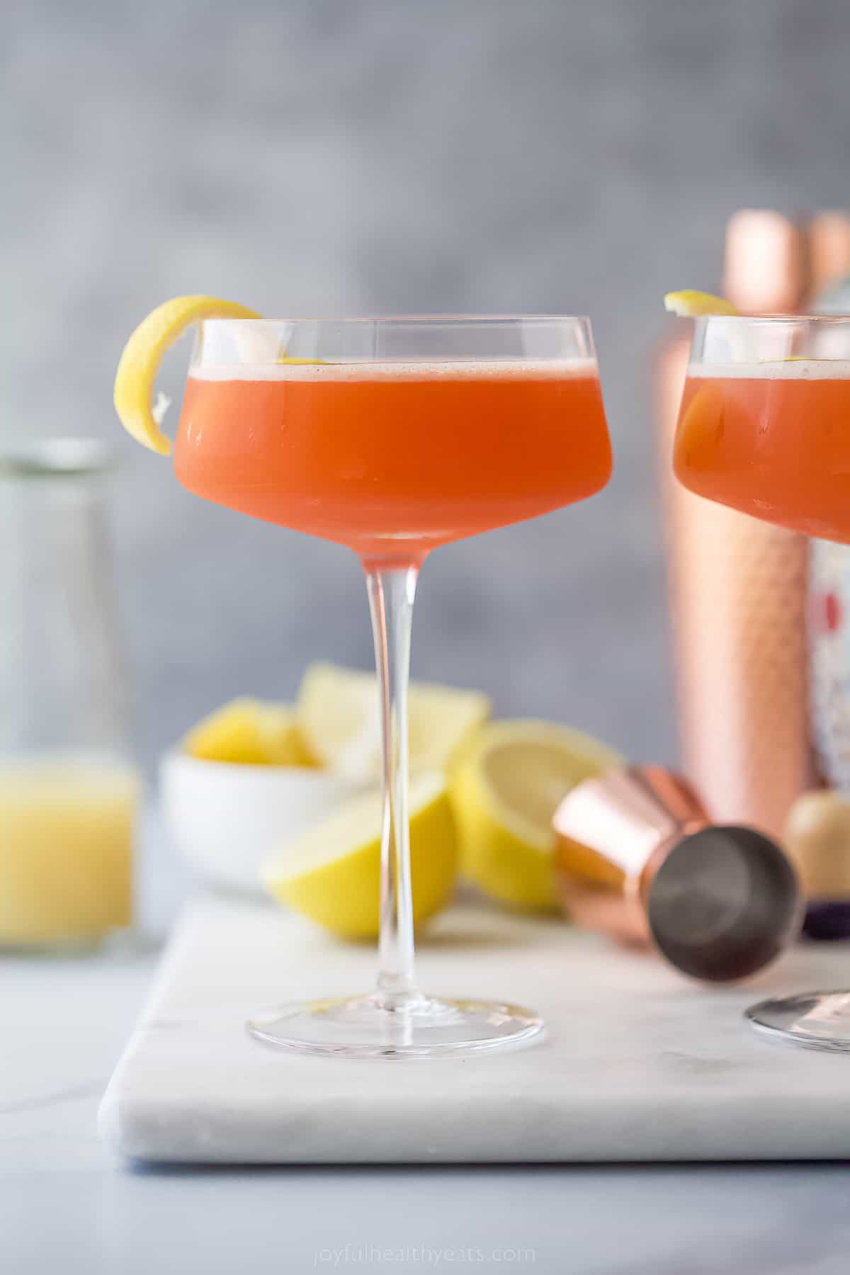 A pale orange paper plane drink with lemon garnish