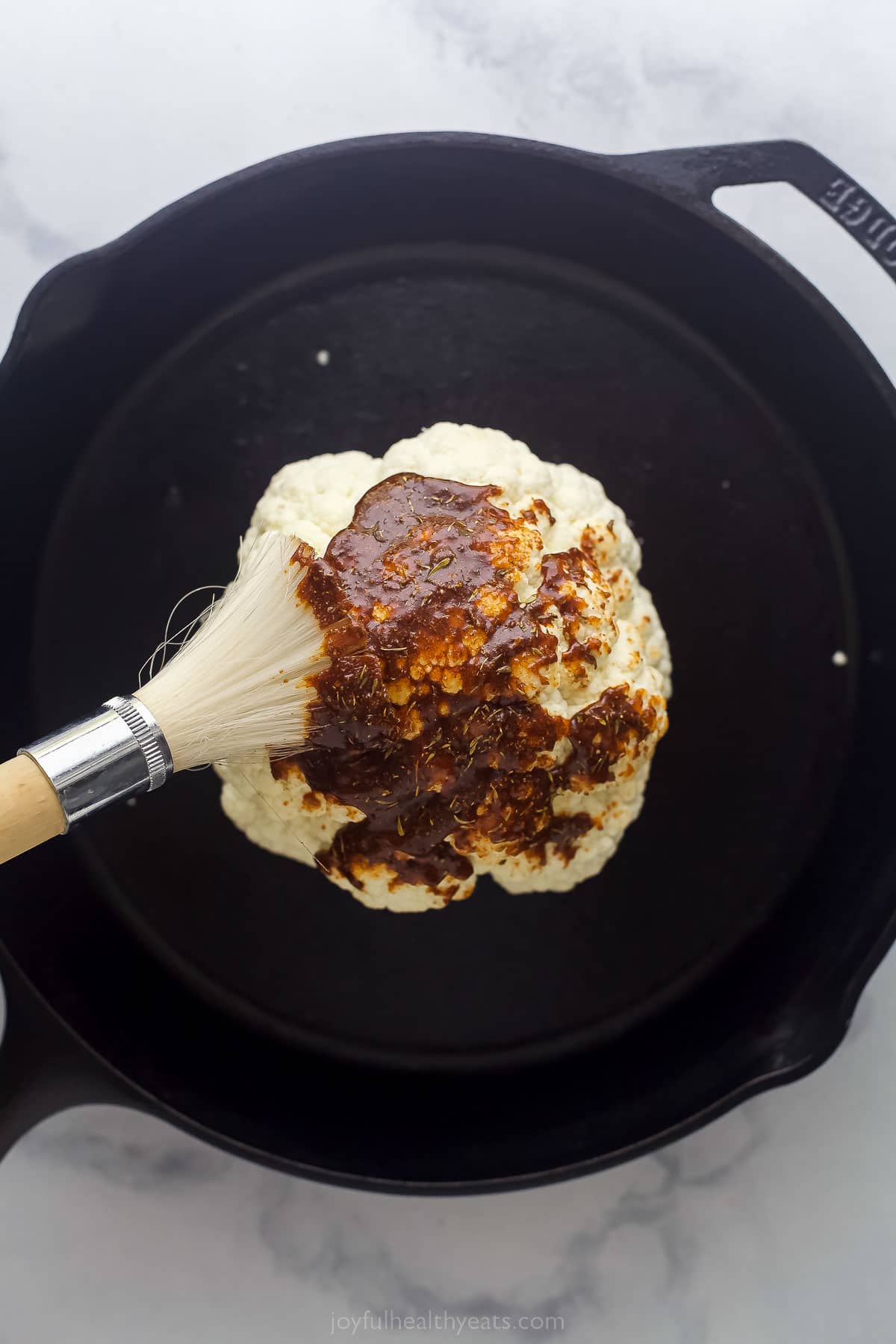 brushing a whole head of cauliflower with dark seasoning