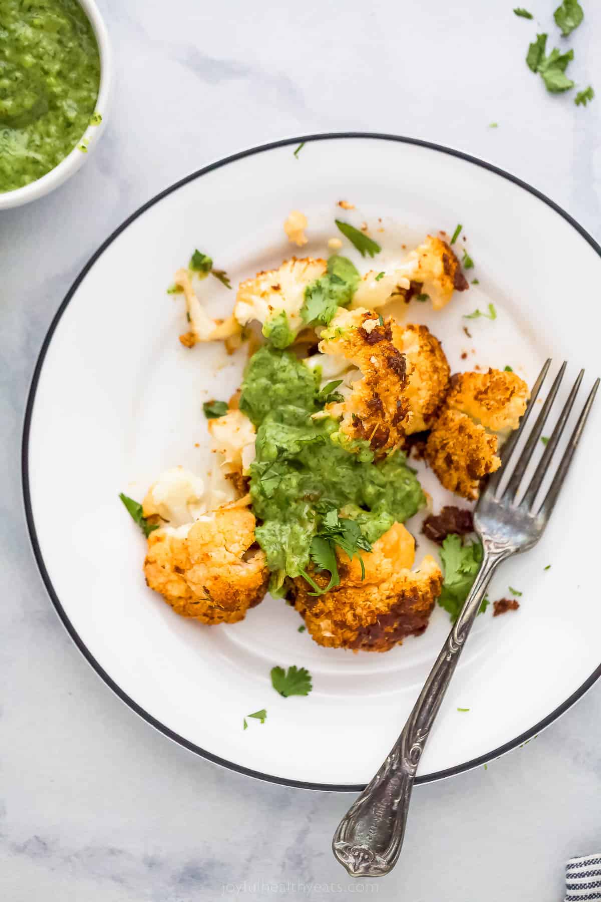 A plate with roasted cauliflower bits and green sauce on top