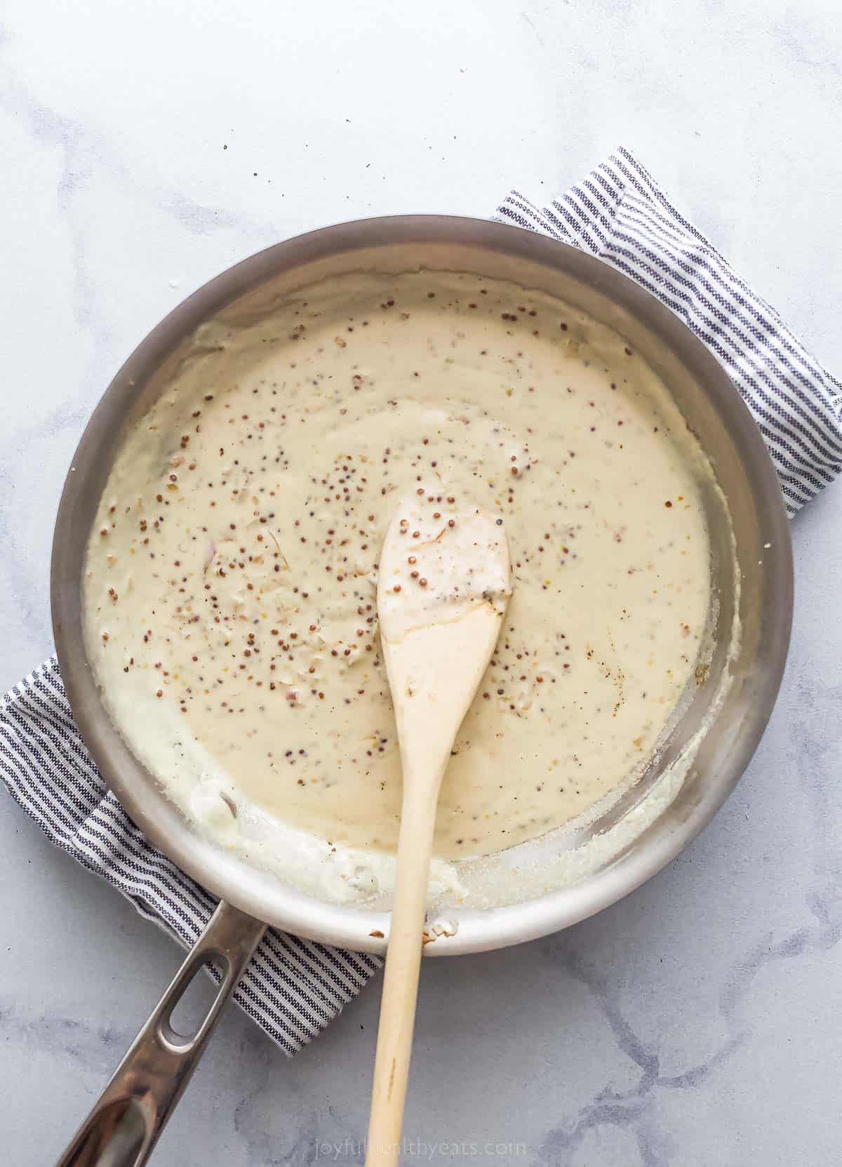 a creamy sauce in a saute pan with a wooden spoon