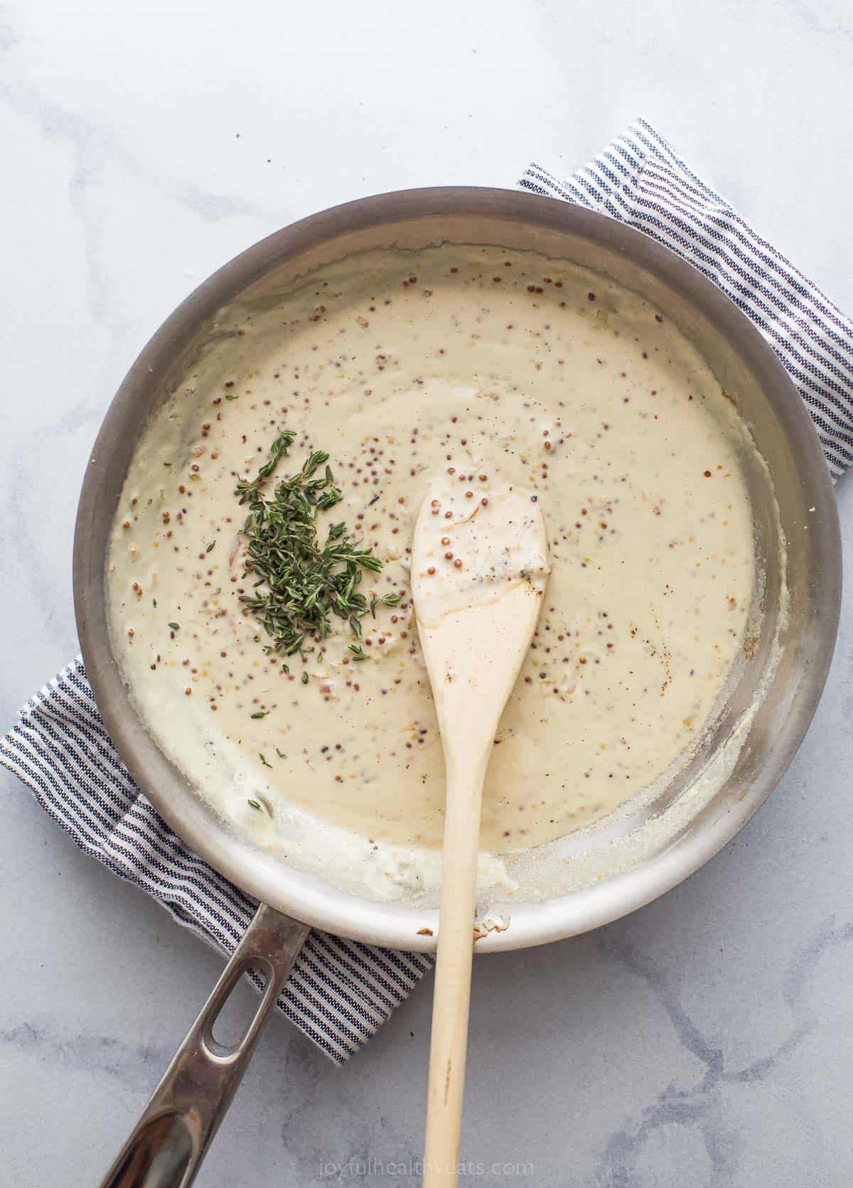 a creamy sauce in a saute pan with a wooden spoon and herbs on top