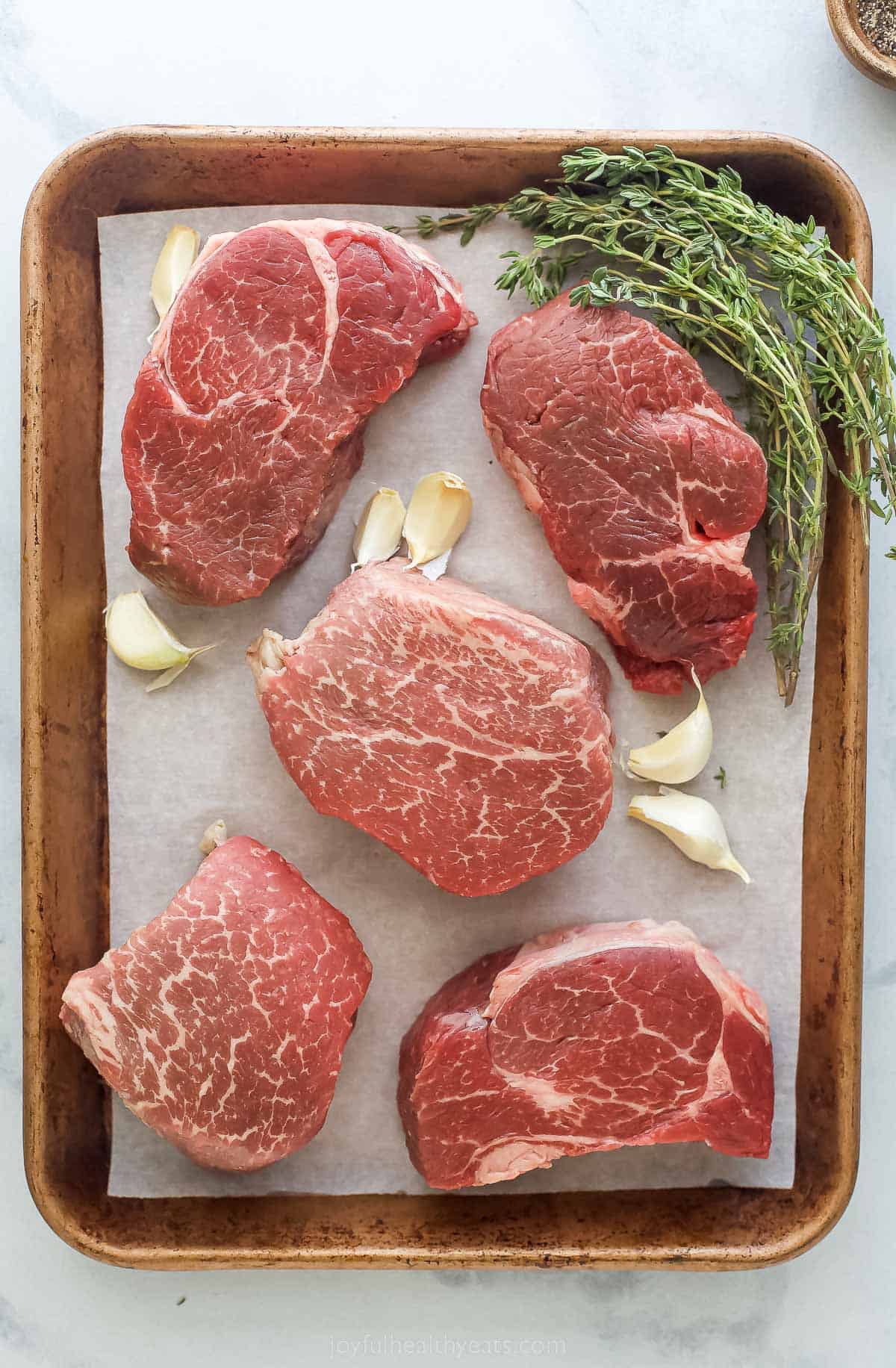 Filet Mignon with Mustard and Mushrooms is an elegant and easy steak dinner with sauteed mushrooms and a creamy dijon sauce. a sheet pan with five filets, garlic, and thyme