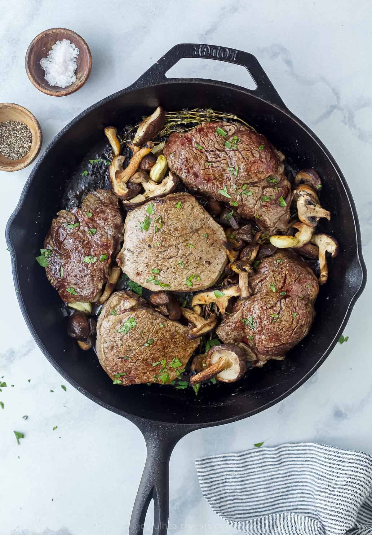 cooked filet mignon in a cast iron skillet with mushrooms and herbs