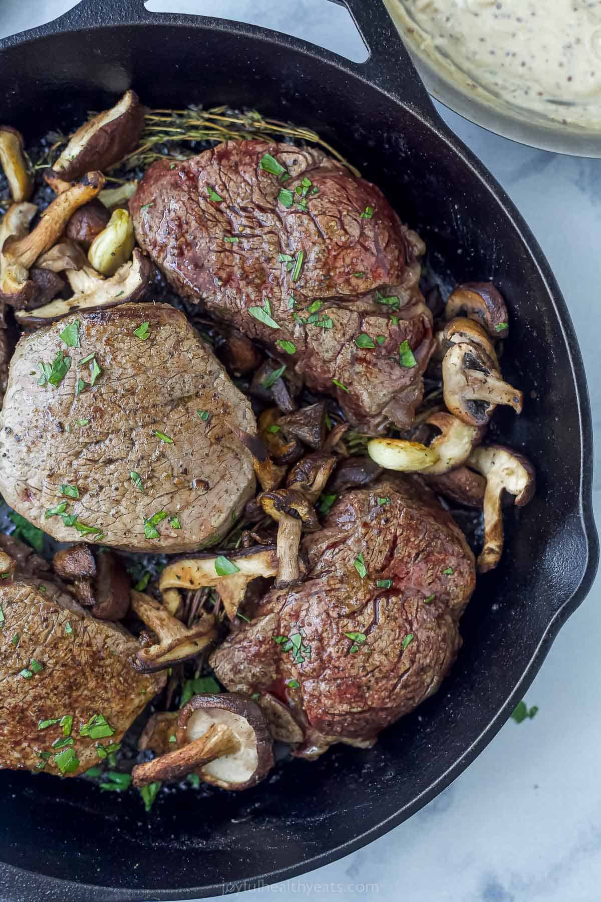 cast iron skillet with filet mignon cuts that have been cooked with mushrooms