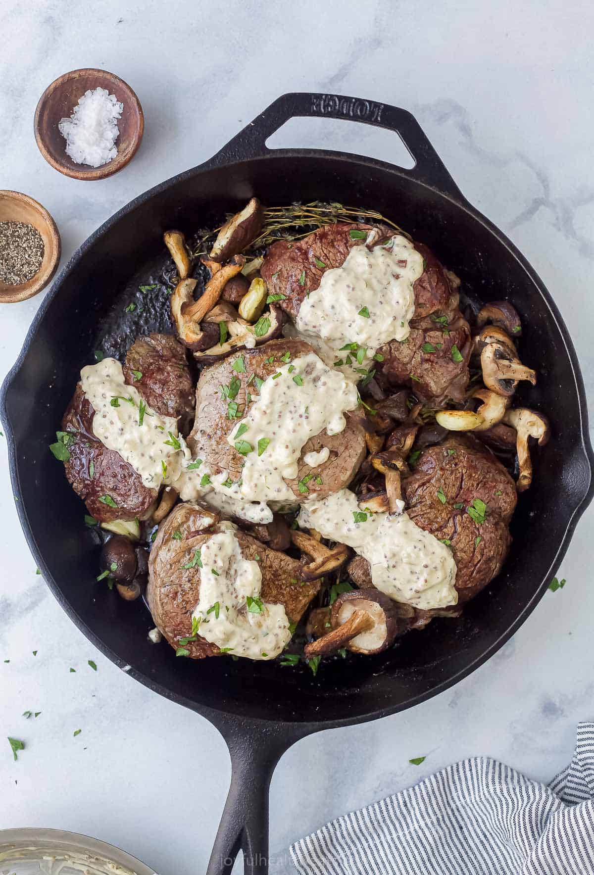 cooked filet mignon in a cast iron skillet with mustard sauce and mushrooms
