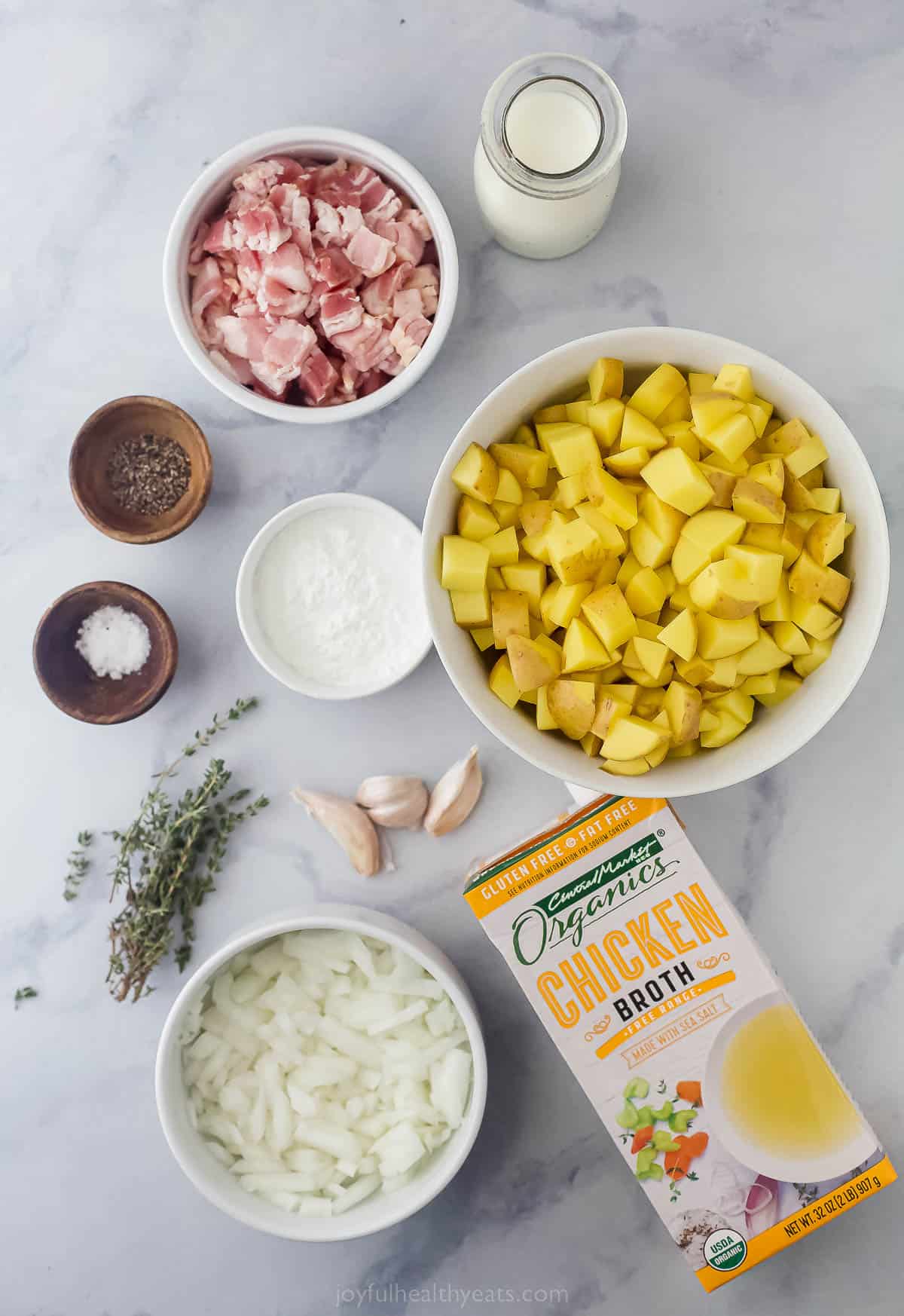 Ingredients to make potato soup like chopped potatoes, bacon, stock, cream, herbs, onions, and seasonings