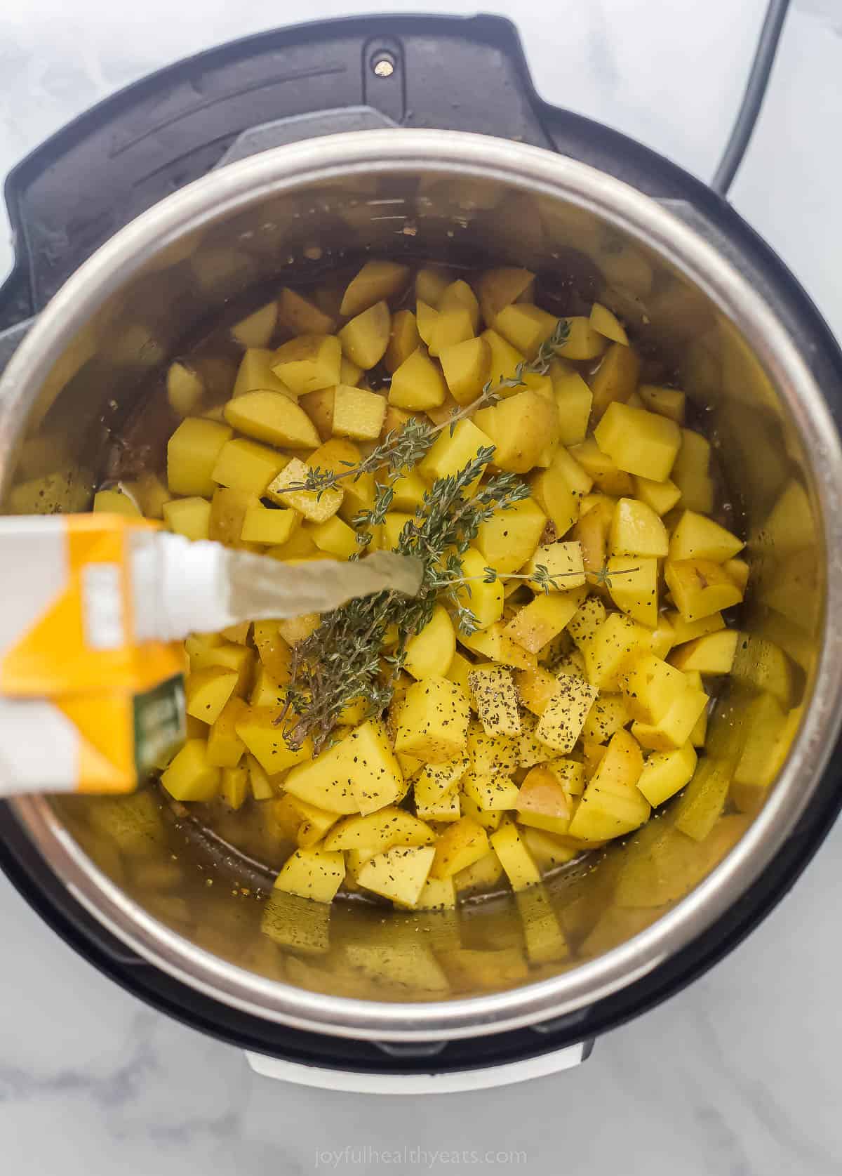 pouring stock into an Instant Pot that has potatoes and herbs in it
