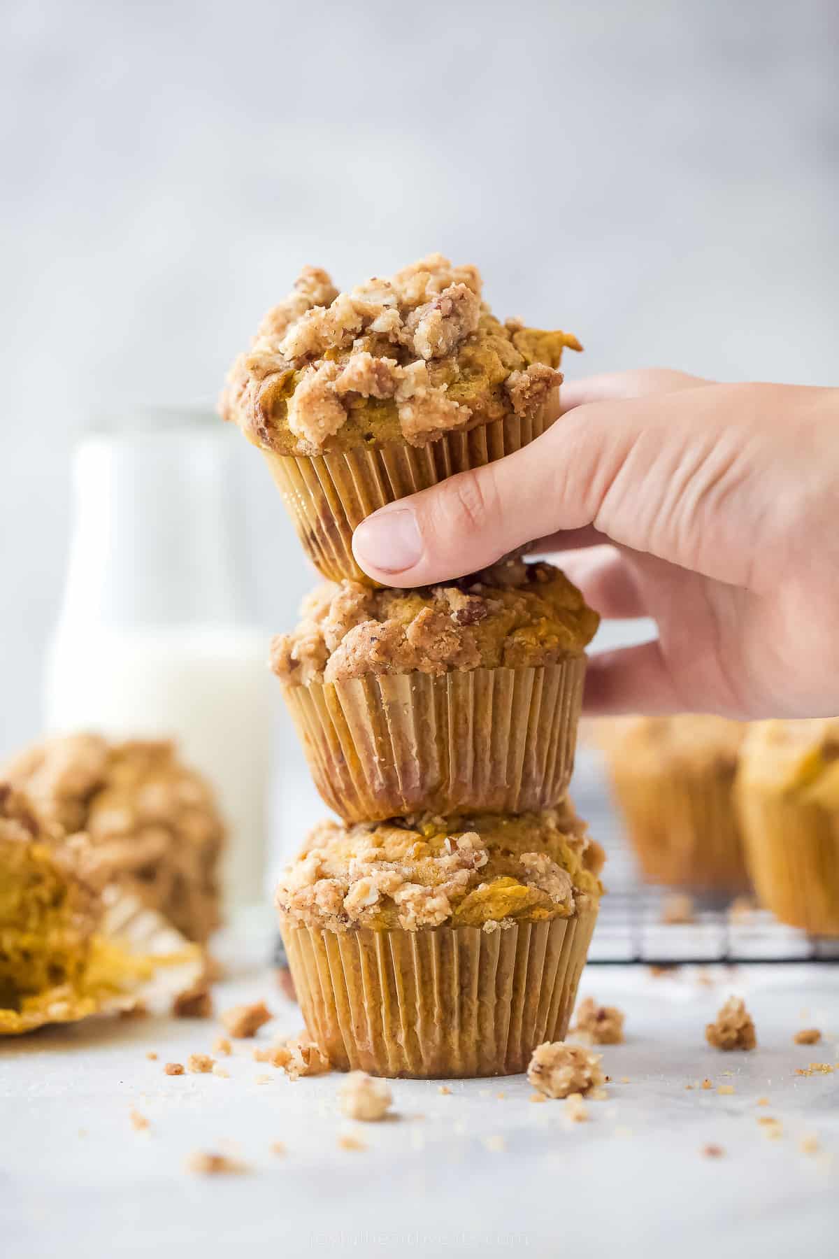 three pumpkin muffins stacked on top of each other with a hand grabbing one
