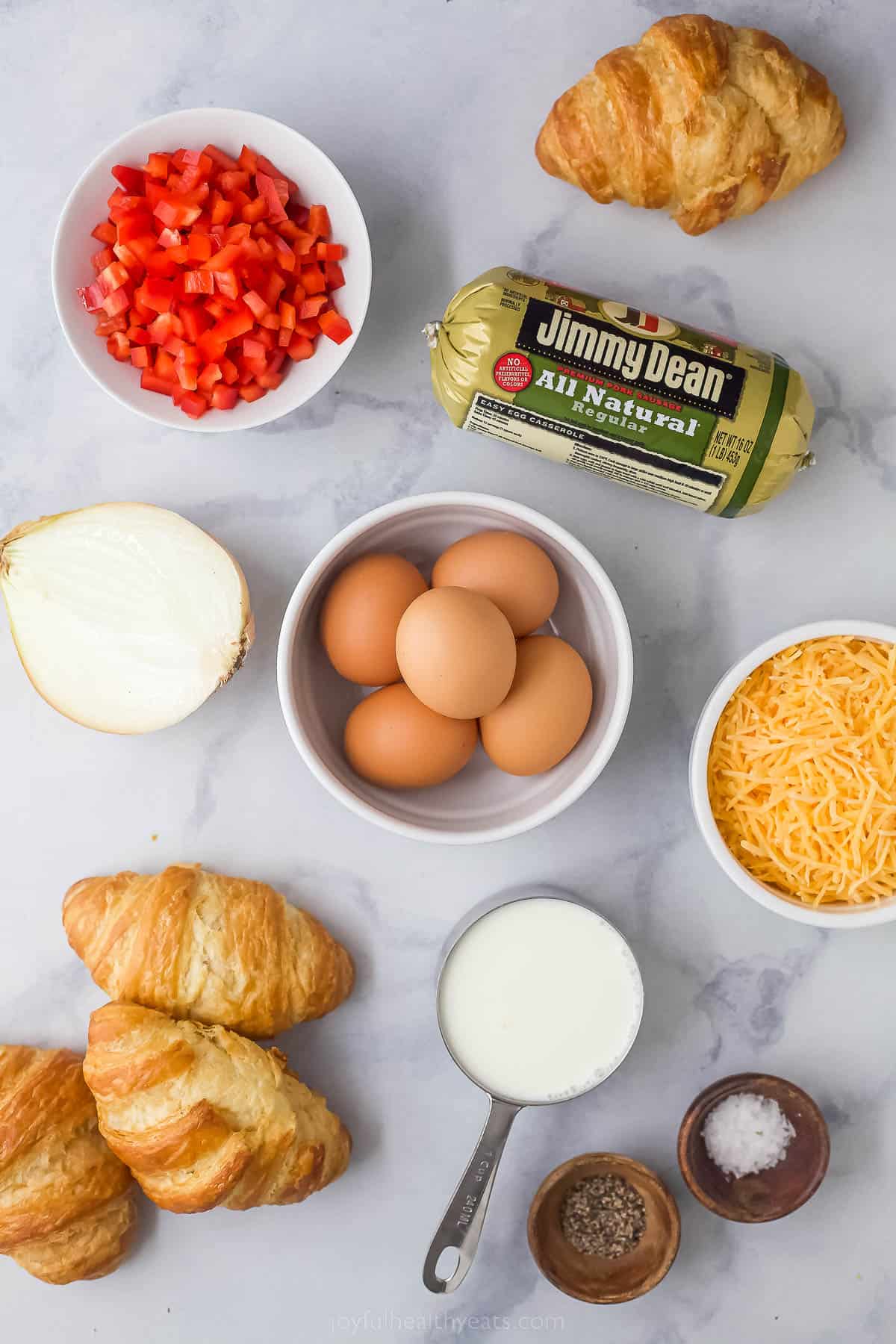 ingredients to make a breakfast casserole like eggs, sausage, cheese, red peppers, croisssants, and cream