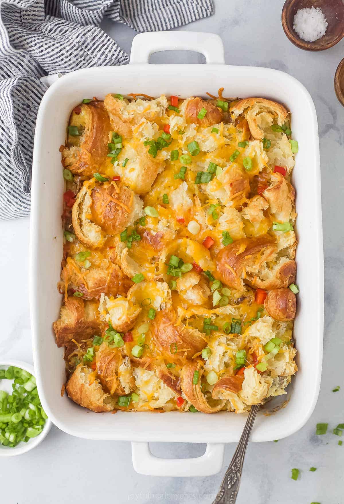 croissant breakfast casserole with eggs, cheese, peppers, green onions, and cheese in a white ceramic dish