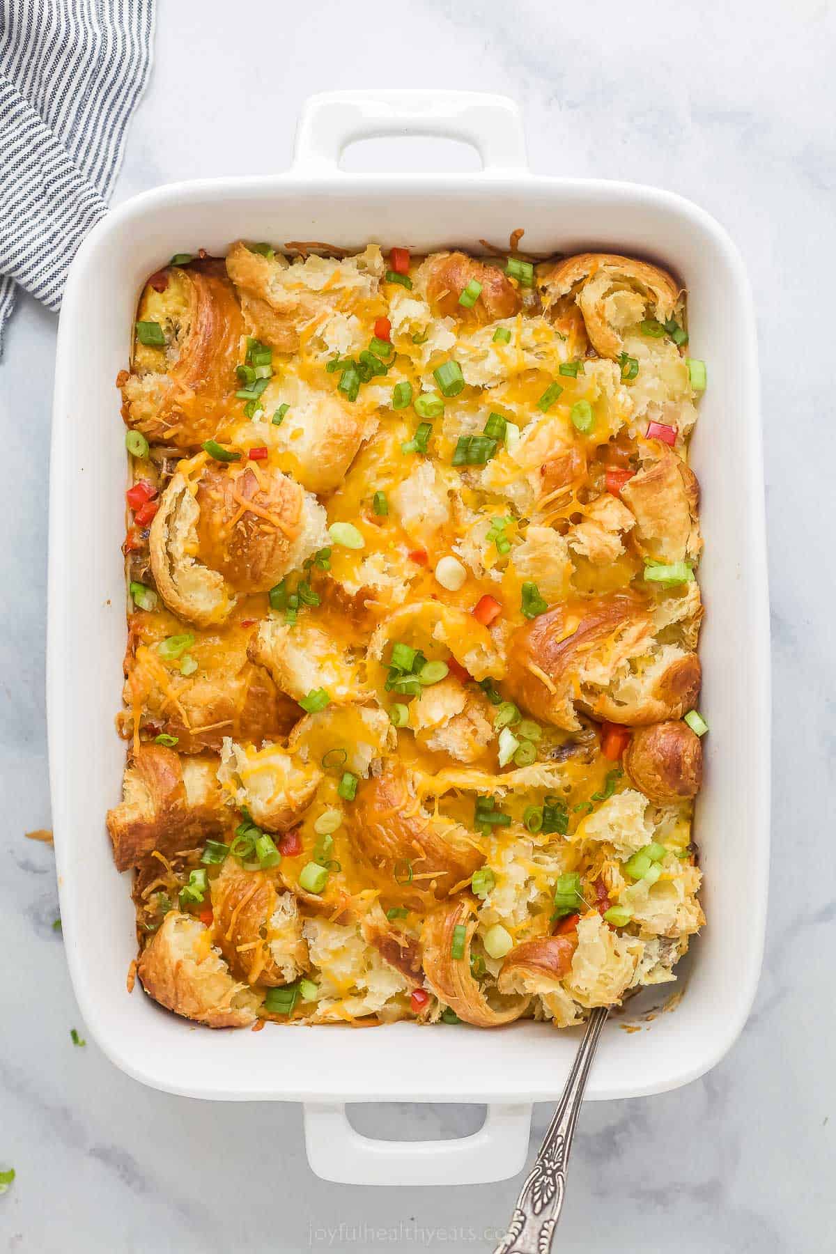 croissant breakfast casserole with eggs, cheese, peppers, green onions, and cheese in a white ceramic dish