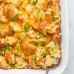 croissant breakfast casserole with eggs, cheese, peppers, green onions, and cheese in a white ceramic dish