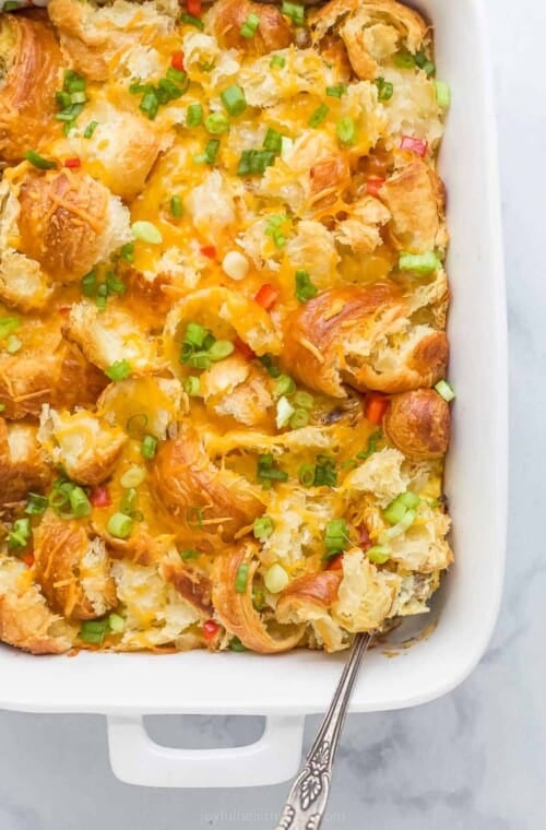 croissant breakfast casserole with eggs, cheese, peppers, green onions, and cheese in a white ceramic dish