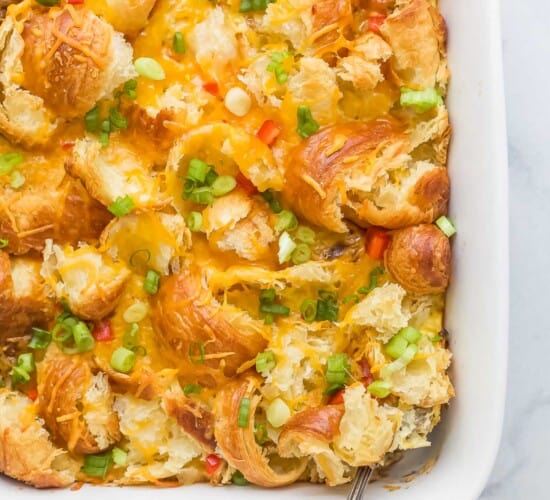 croissant breakfast casserole with eggs, cheese, peppers, green onions, and cheese in a white ceramic dish