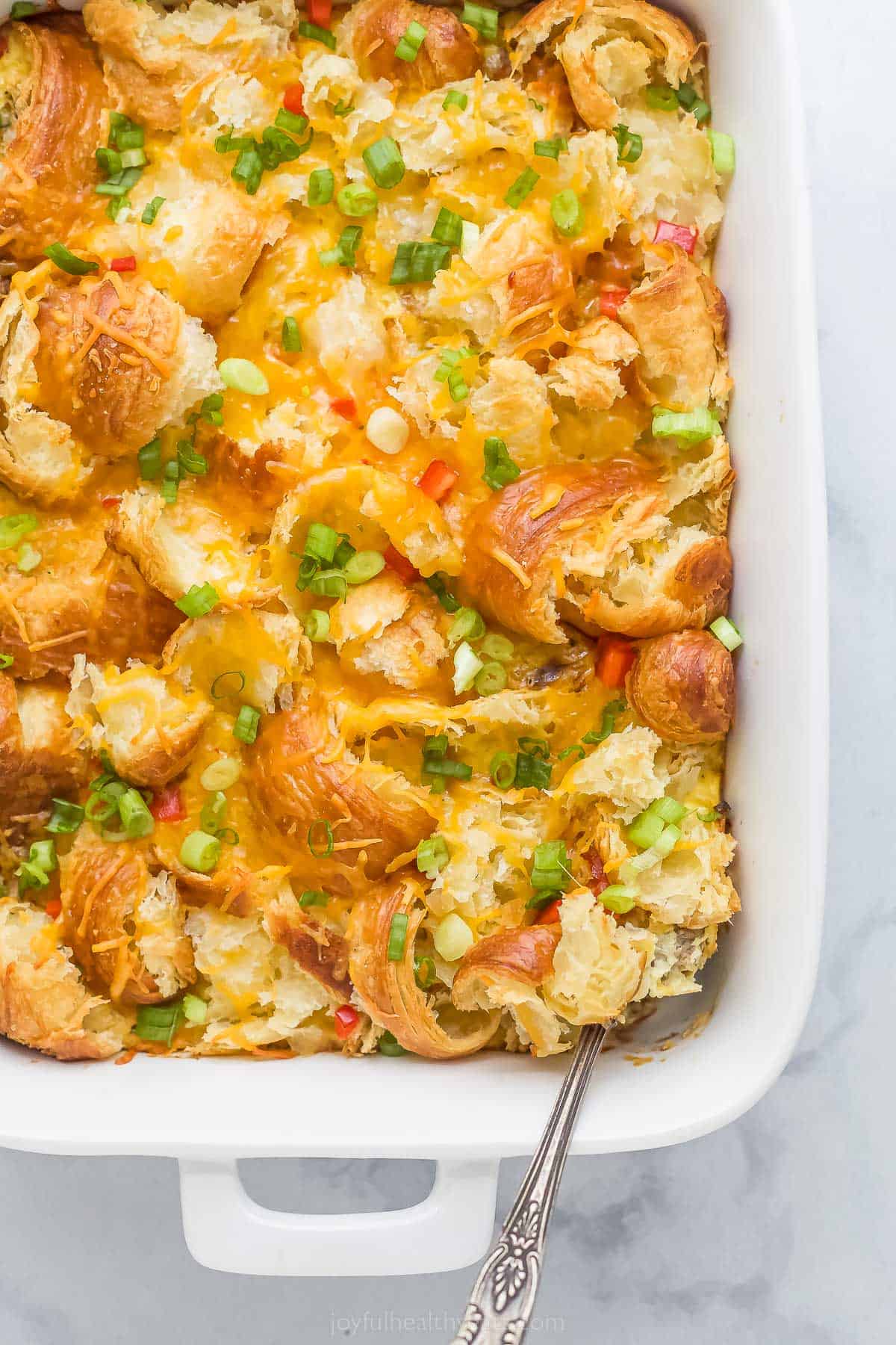 croissant breakfast casserole with eggs, cheese, peppers, green onions, and cheese in a white ceramic dish