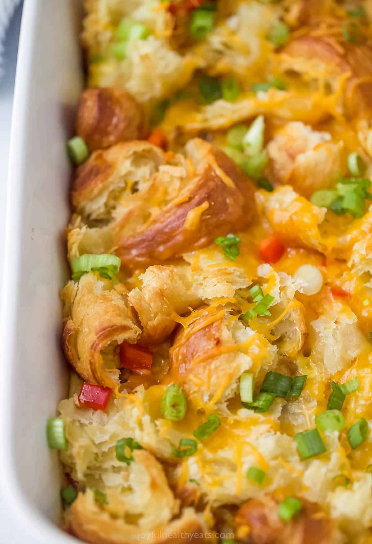close up of a breakfast casserole made with cut up croissants, sausage, cheese, green onions, and red peppers