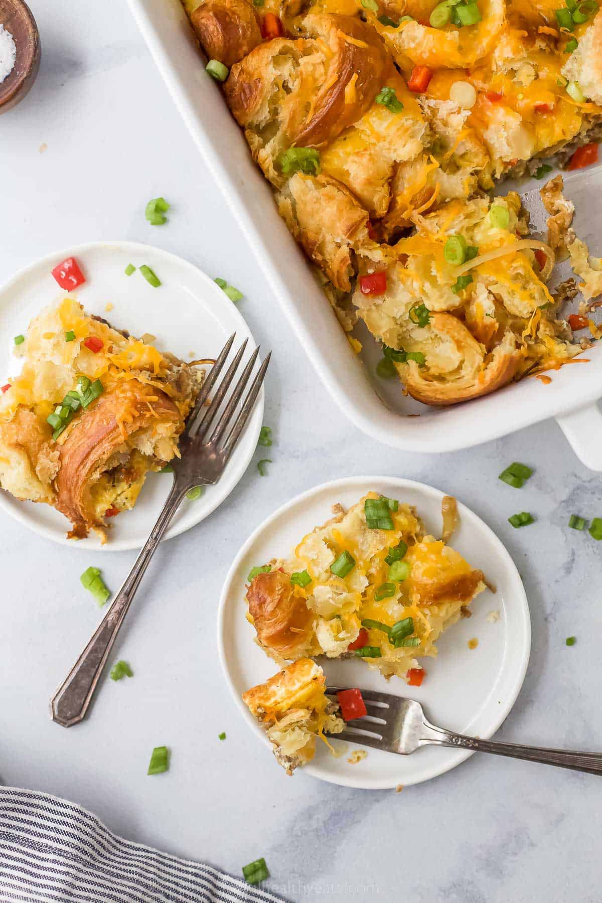 two plates next to a casserole dish with croissant breakast bake with sausage