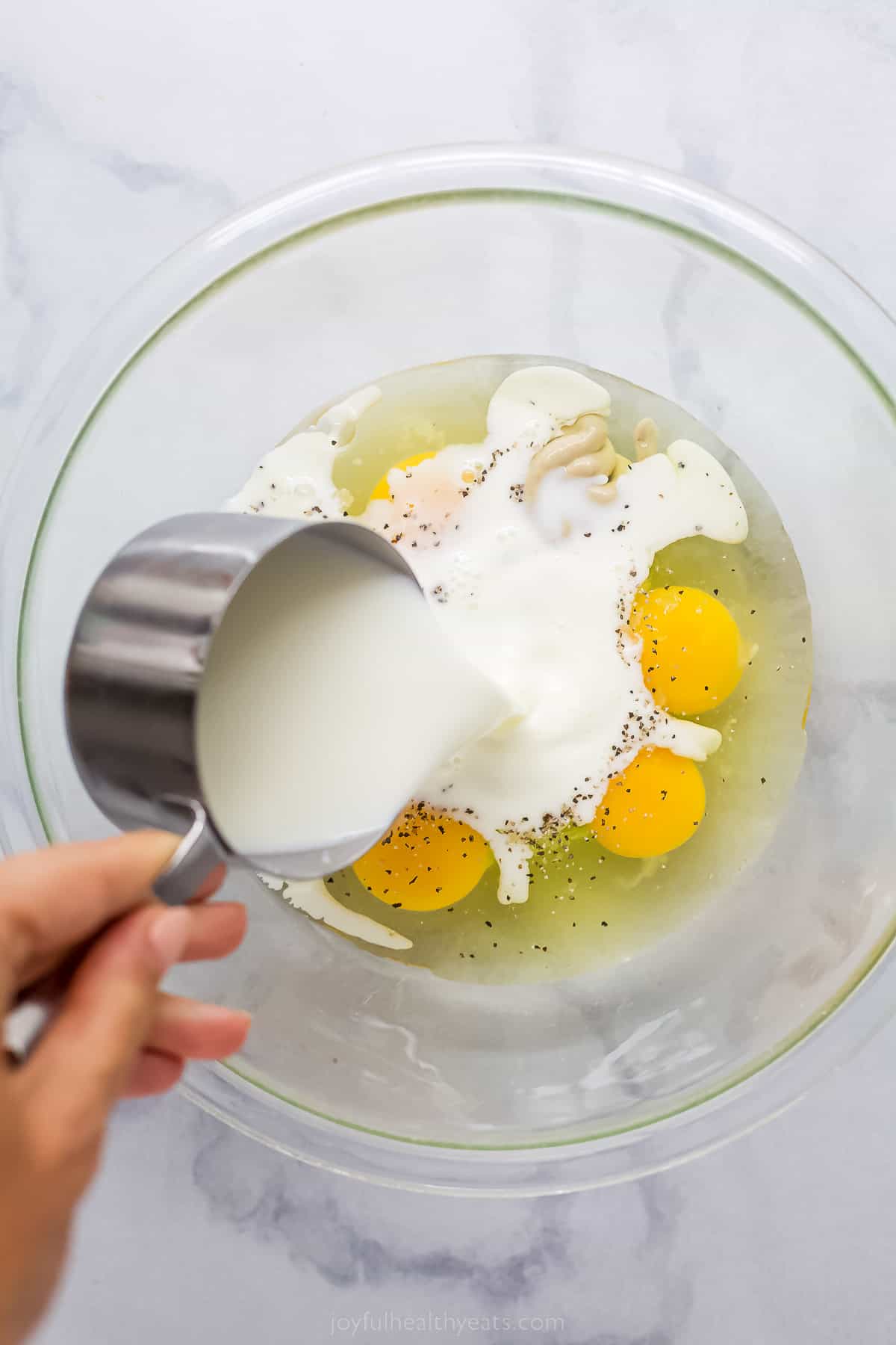 pouring cream into a bowl with cracked eggs