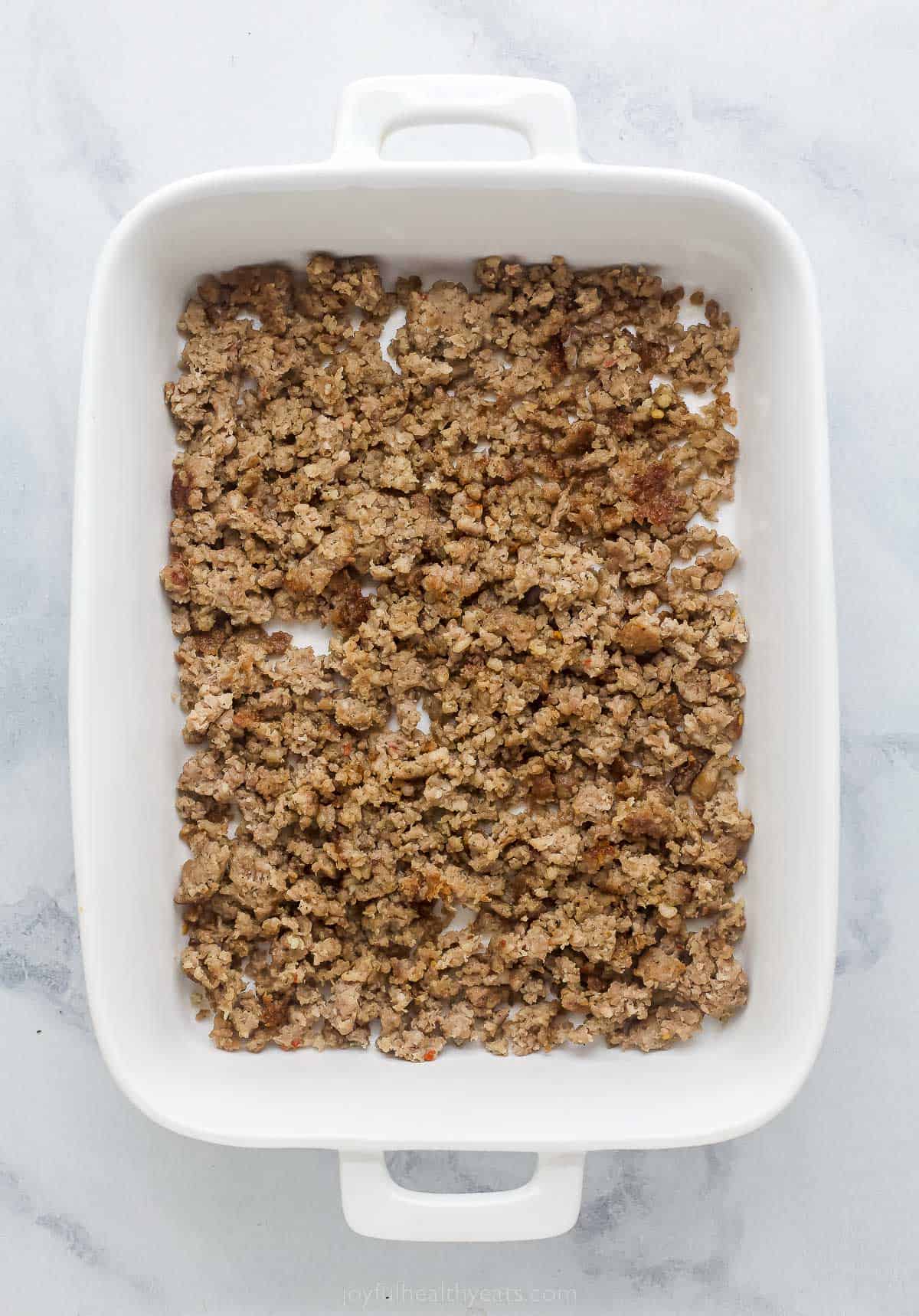 a casserole dish with a thin layer of cooked sausage on the bottom