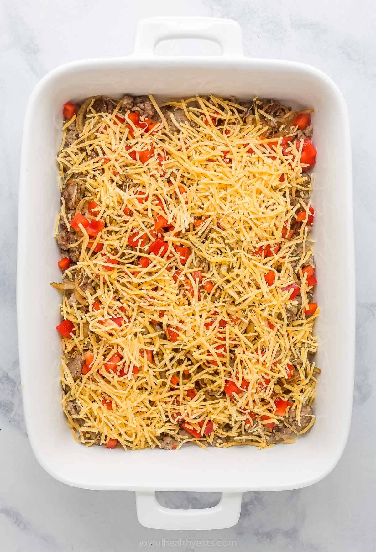 a casserole dish with shredded cheese, red peppers, and sausage