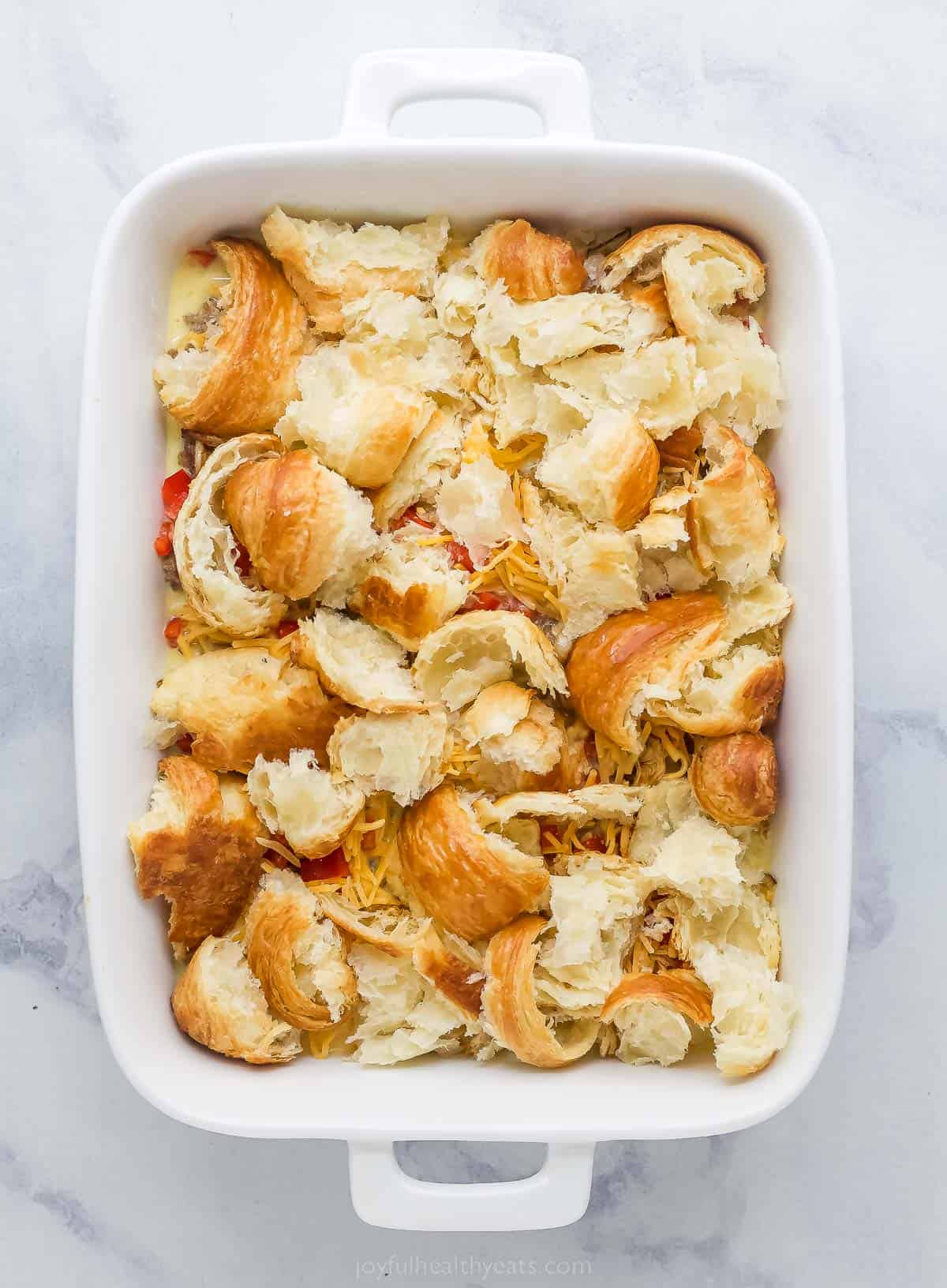a white casserole dish with cut up croissants in it