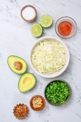 Ingredients to make a creamy slaw like cabbage, avocados, herbs, and lime juice