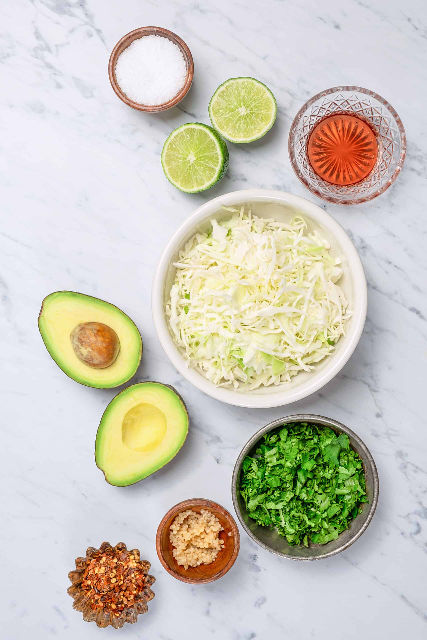 ingredients to make a creamy slaw like cabbage, avocados, herbs, and lime juice