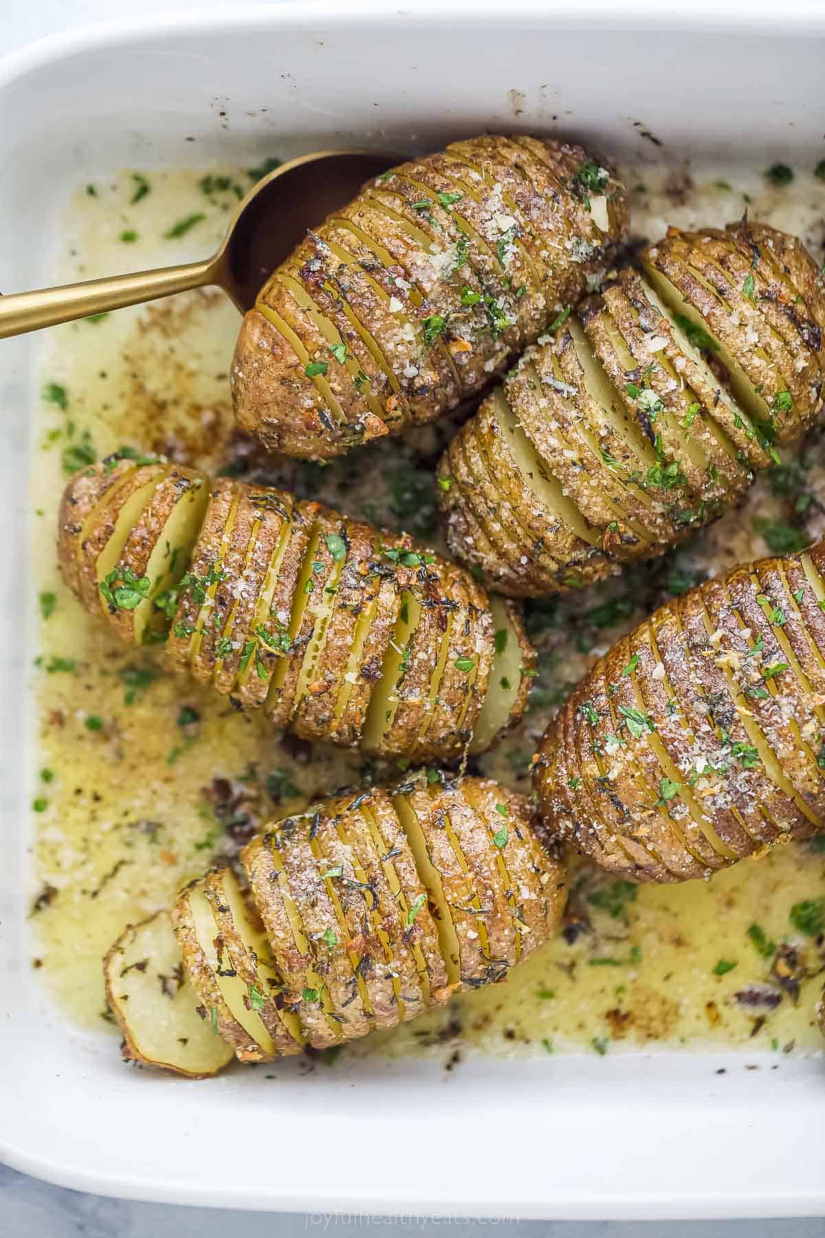 whole potatoes with thin slices with garlic and herbs on top in a baking dish