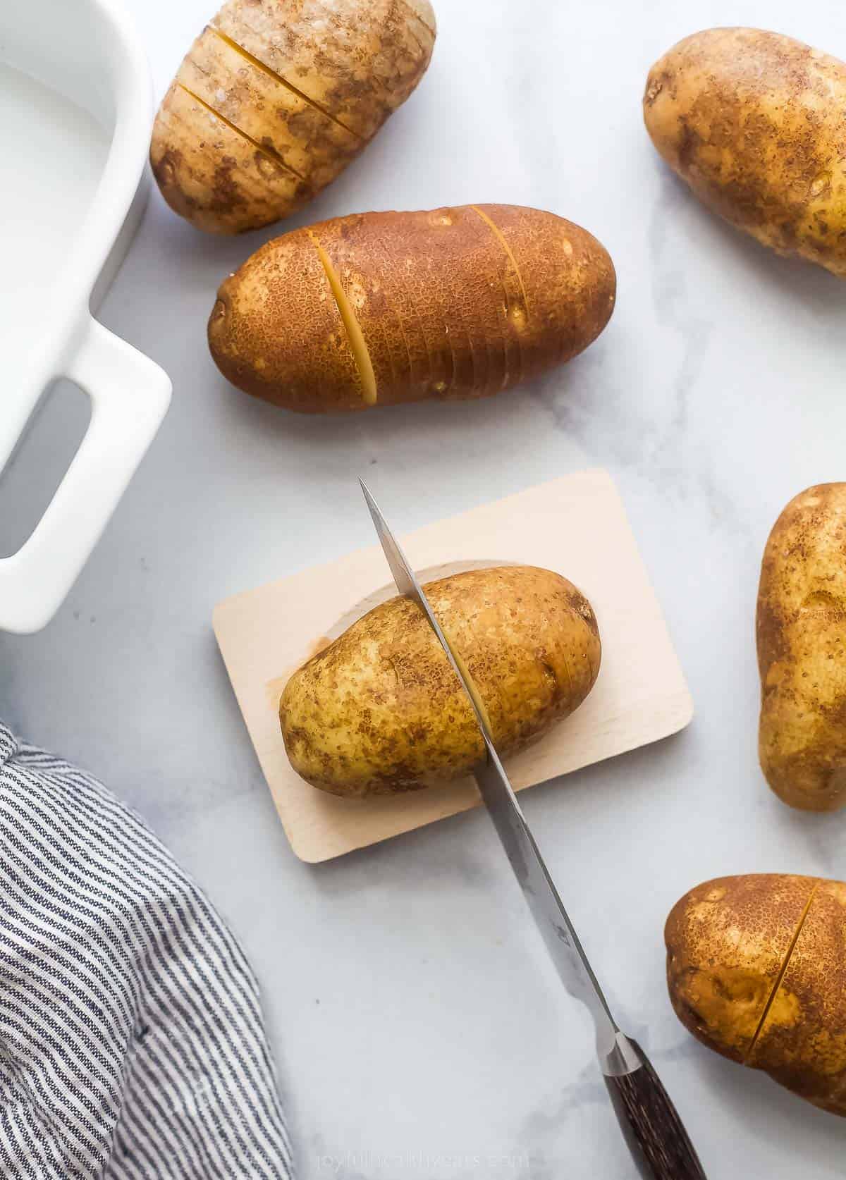 using a knife to cut thin slices into whole potatoes