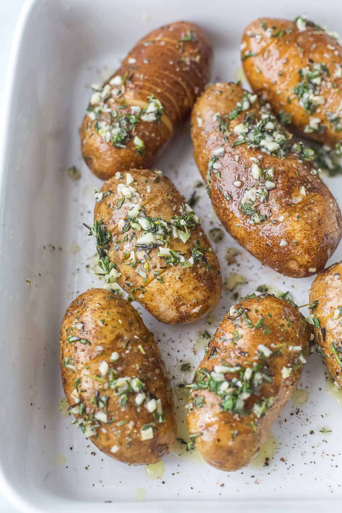 potatoes that have a buttery and herb mixture on top on a casserole dish