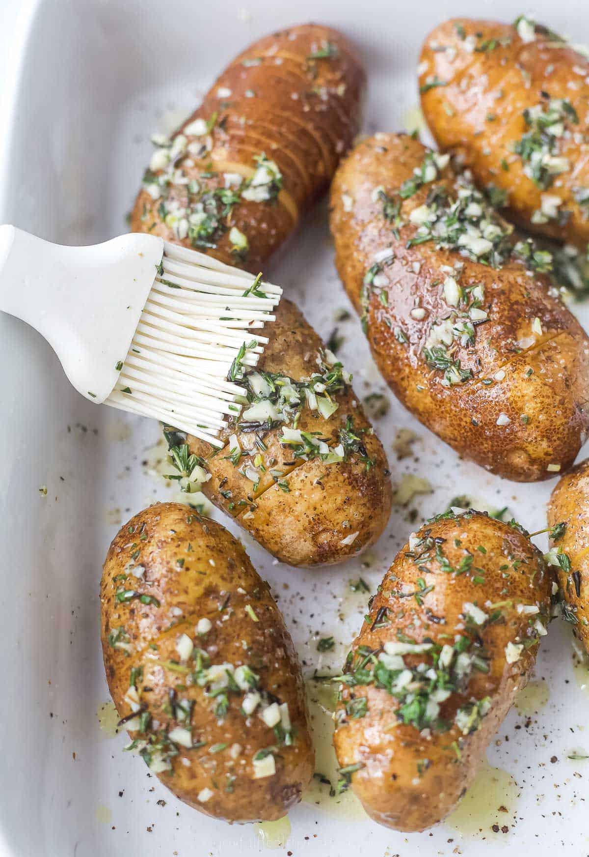 brushing melted butter and herbs onto whole potatoes