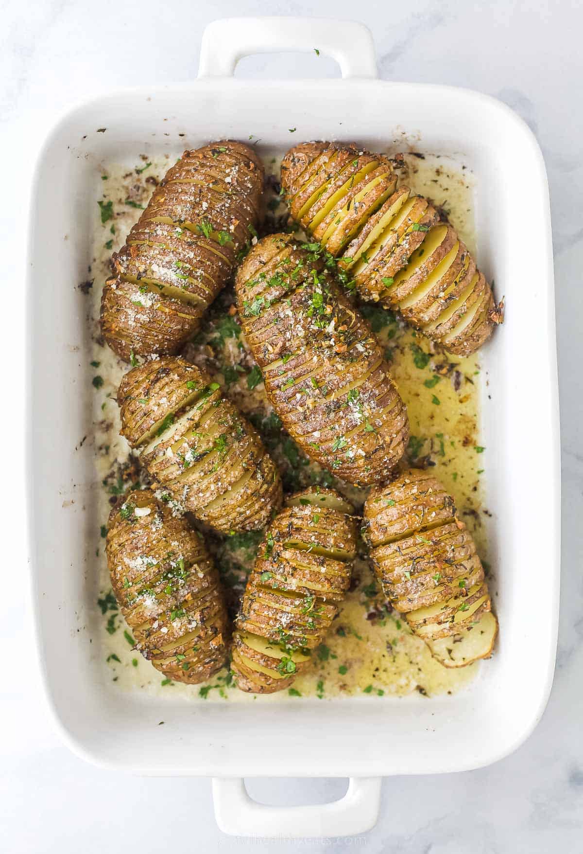 cooked hasselback potatoes in a white casserole dish with herbs and butter on top