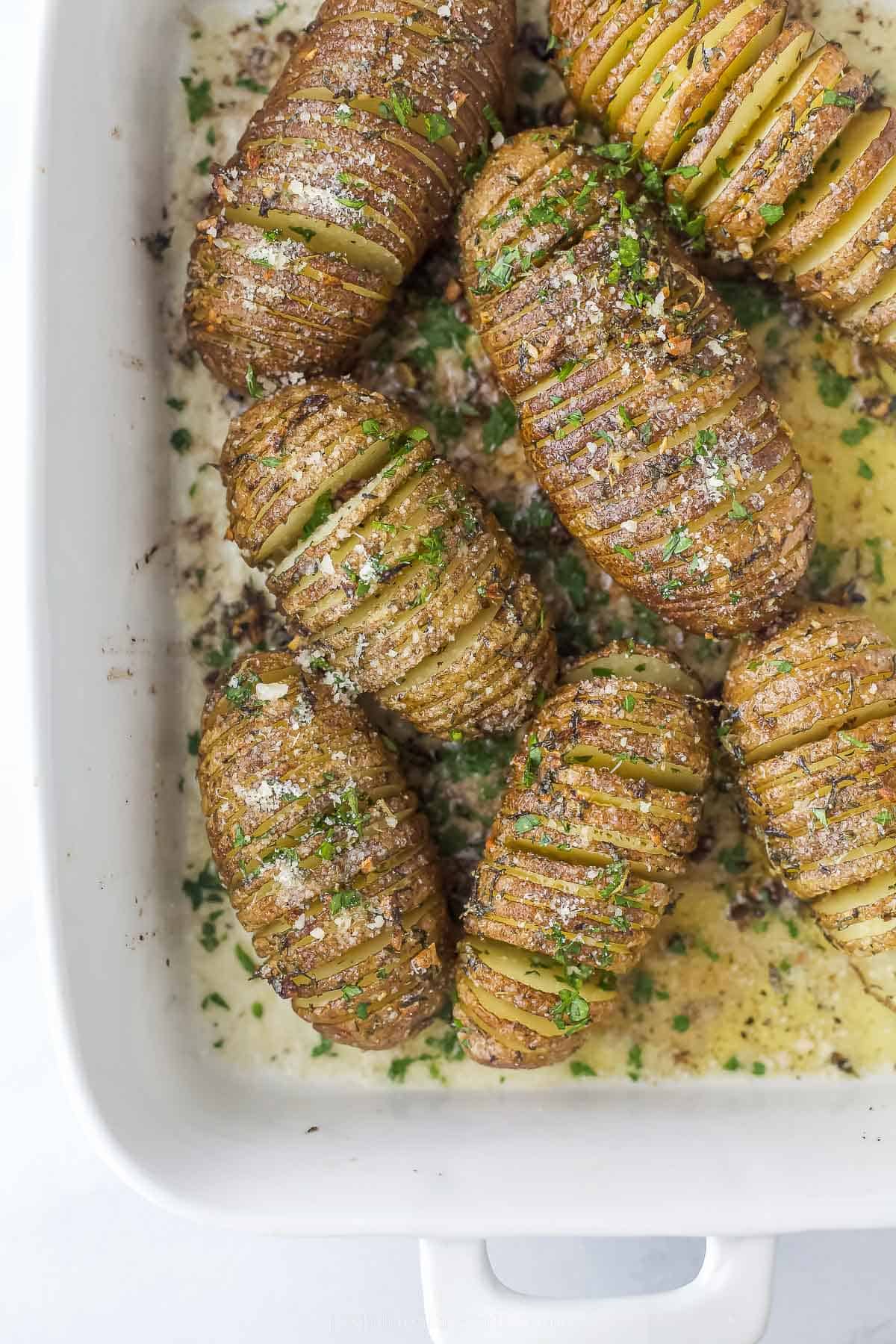 cooked hasselback potatoes in a white casserole dish with herbs and butter on top