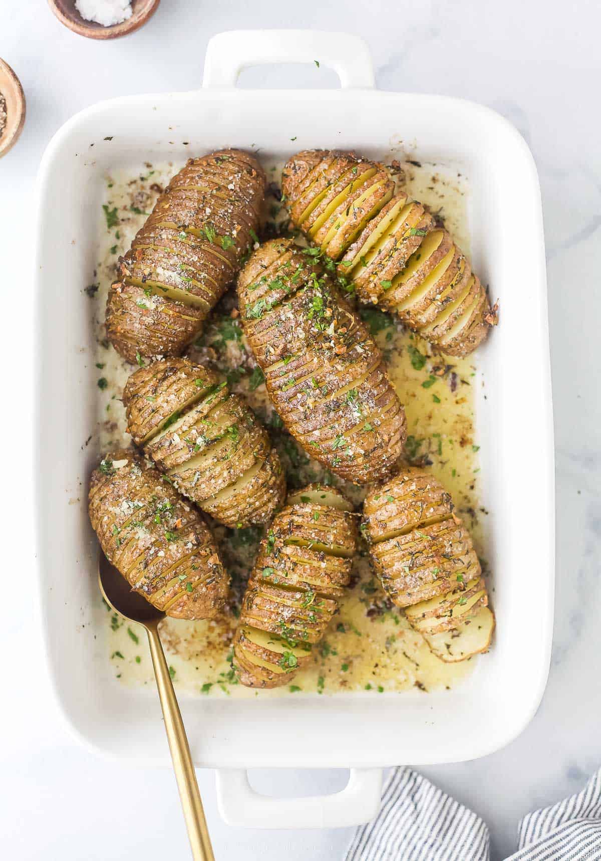 whole potatoes with thin slices with garlic and herbs on top in a baking dish