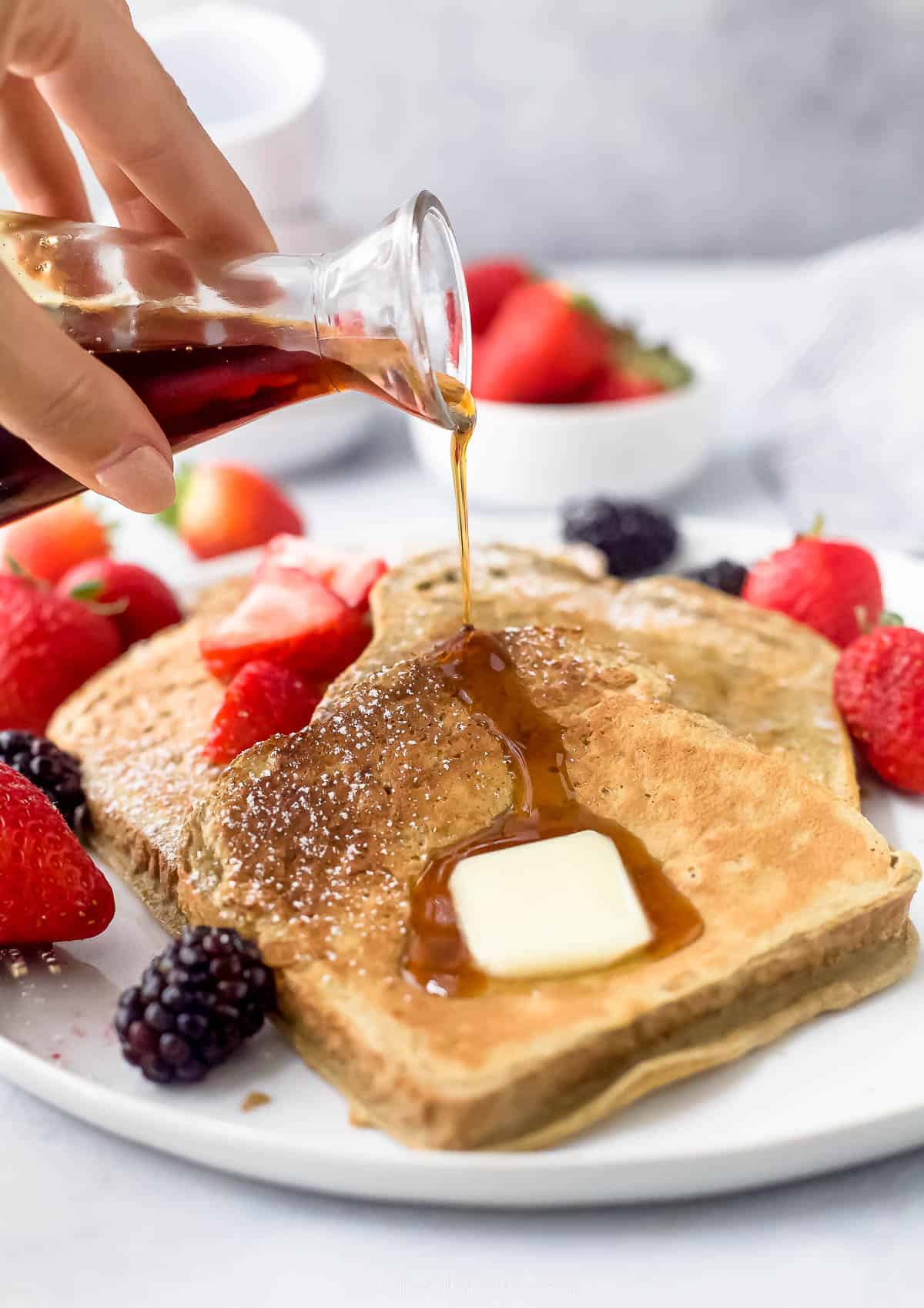 a plate of sliced french toaste with berries, butter, and maple syrup