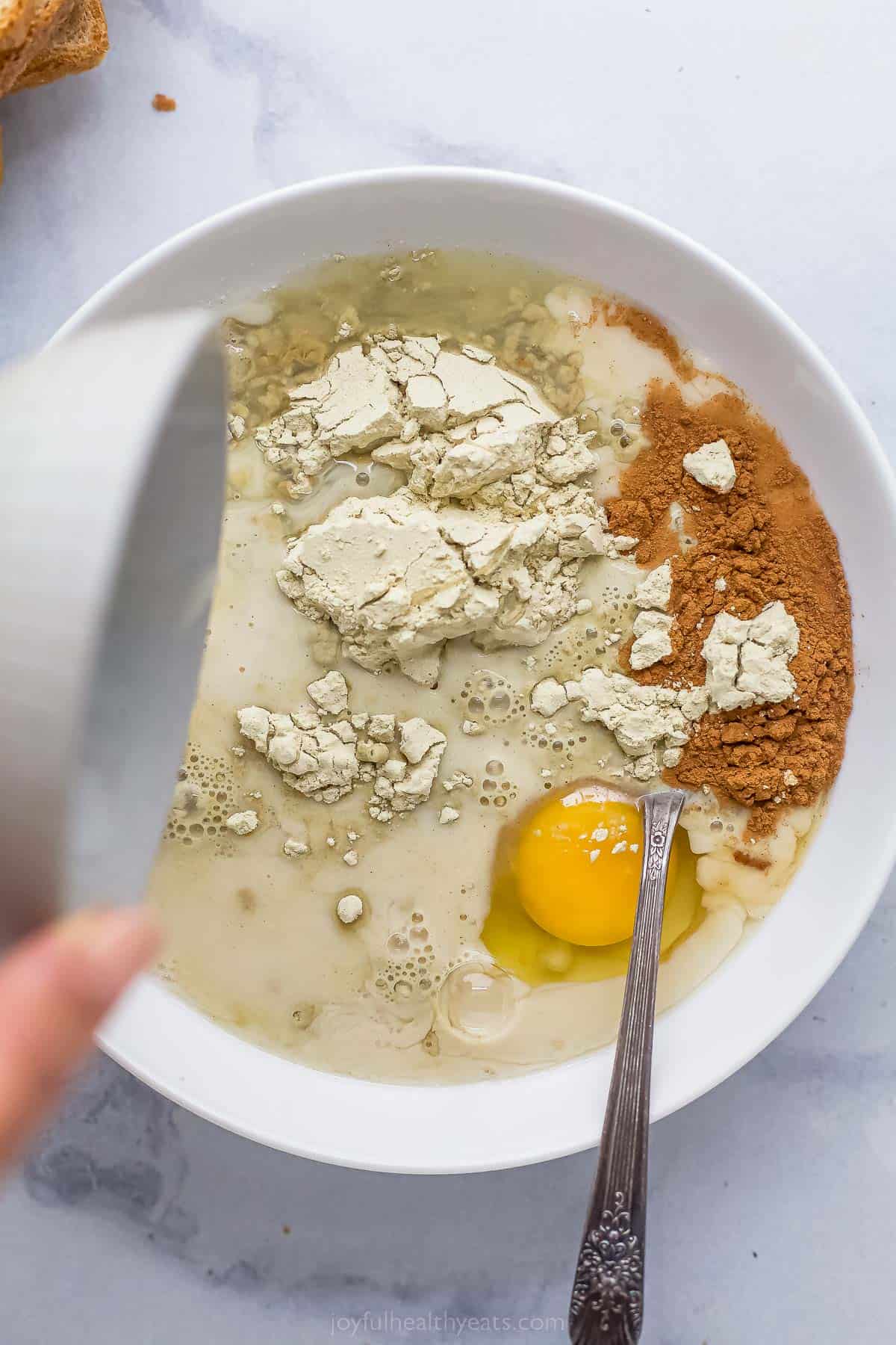 adding protein powder to a bowl with cinnamon, oat milk, and egg