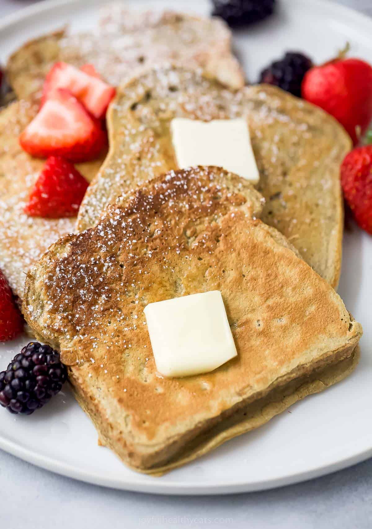 a plate of sliced french toaste with berries, butter, and maple syrup