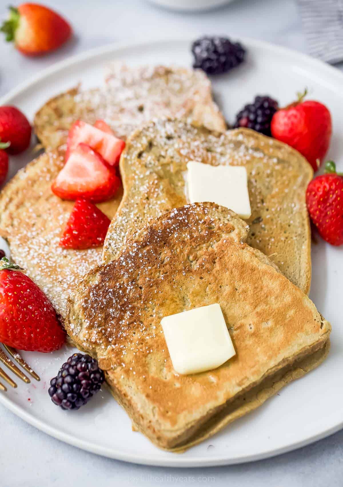 a plate of sliced french toaste with berries, butter, and maple syrup