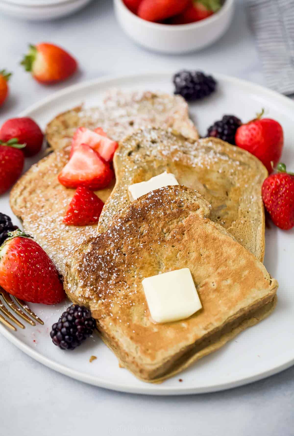 a plate of sliced french toaste with berries, butter, and maple syrup