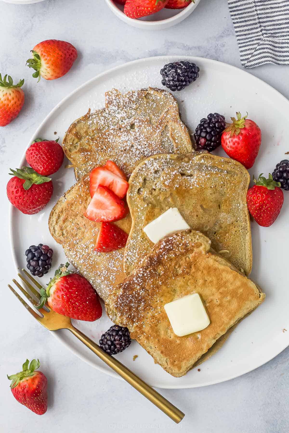 a plate of sliced french toaste with berries, ،er, and maple syrup